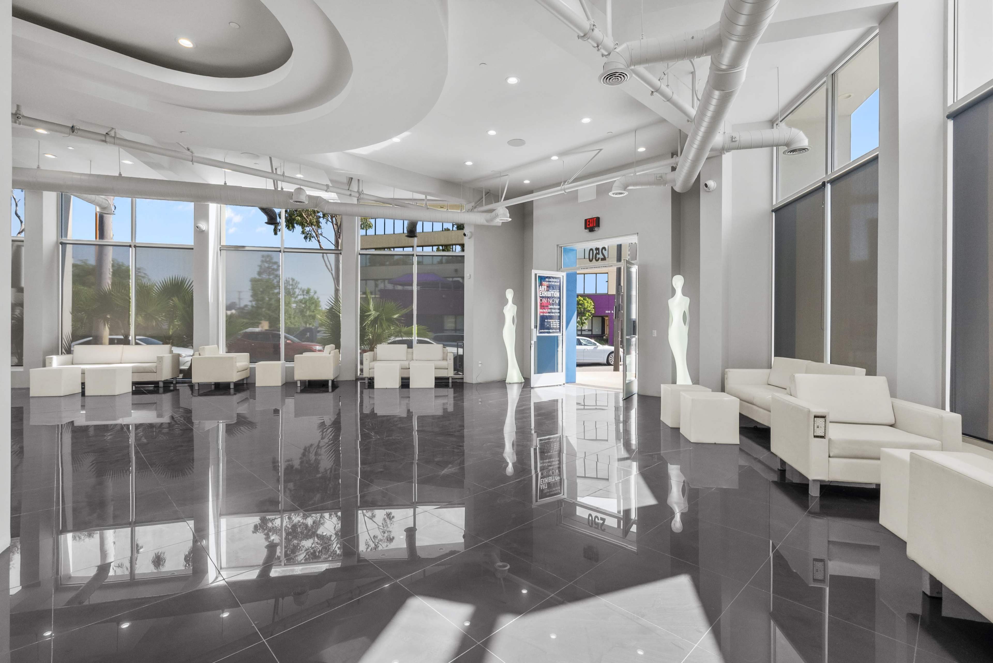 The image shows a modern lobby area with glossy tile flooring, white seating, and large windows allowing natural light to enter.