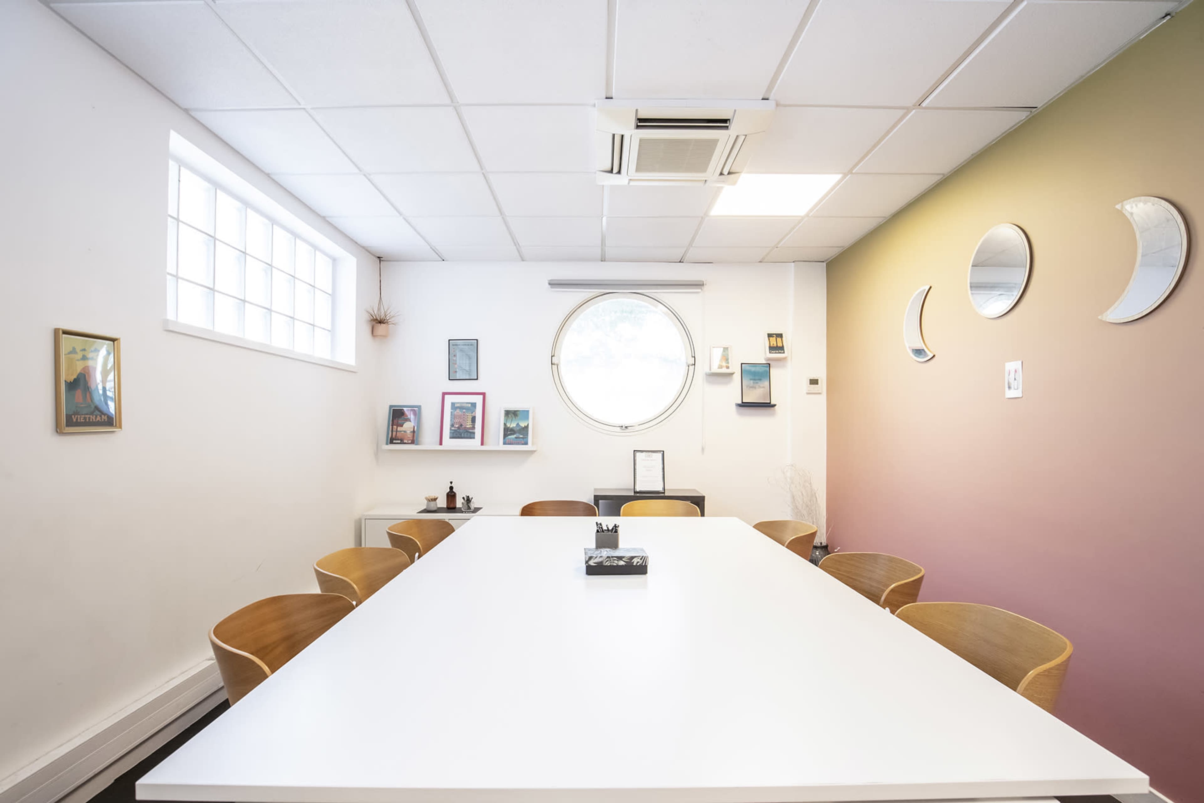 A conference room features a large white table surrounded by wooden chairs, with framed artwork and circular mirrors on the walls.