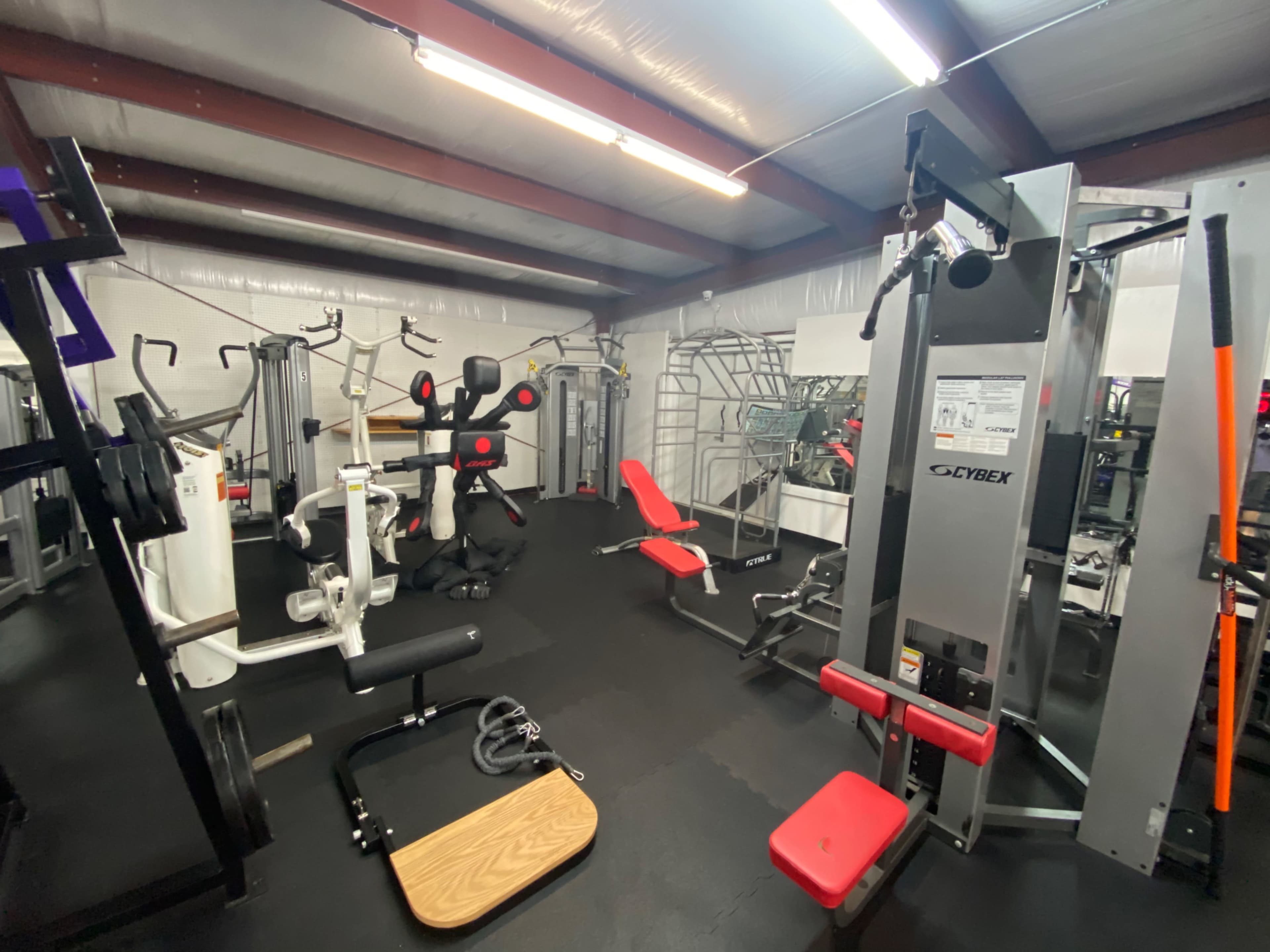 A gym interior equipped with various exercise machines and free weights.