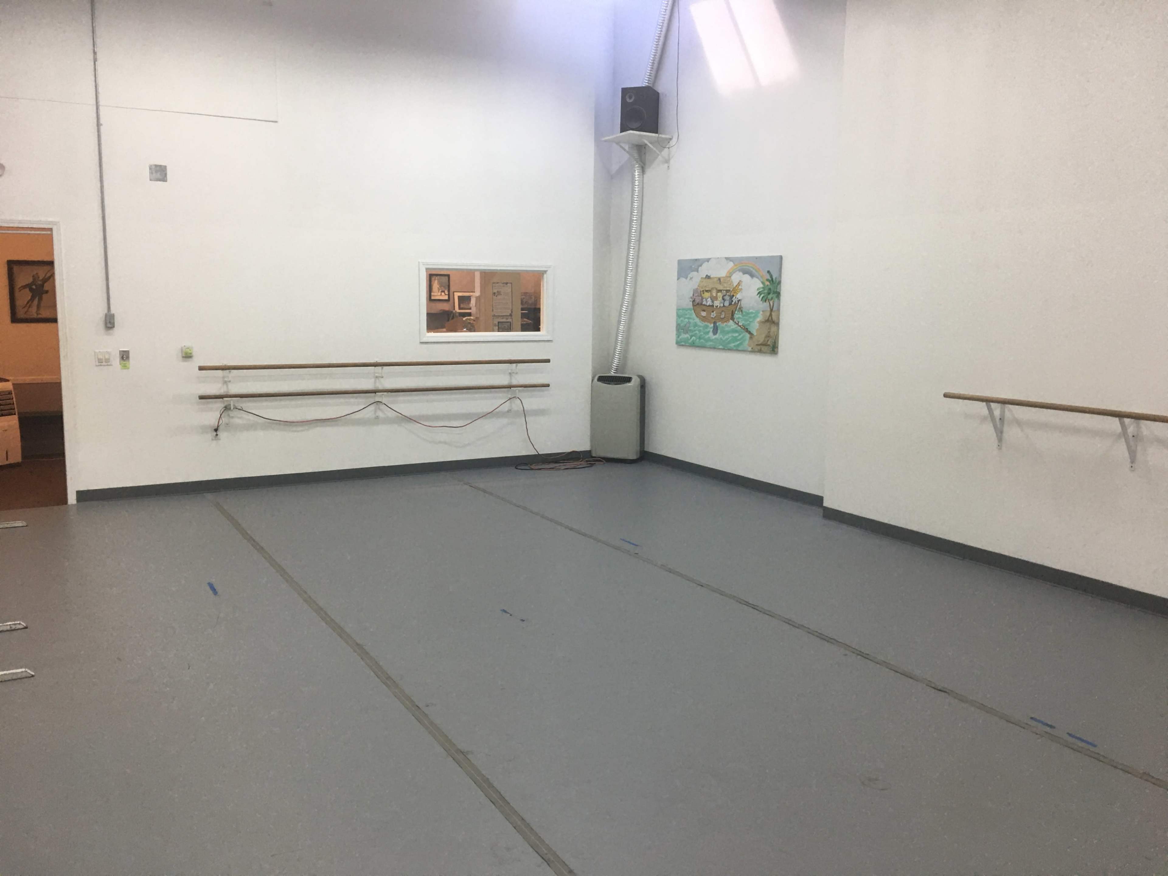 A spacious, empty dance studio with mirrored walls, ballet bars, and a painting on one wall.