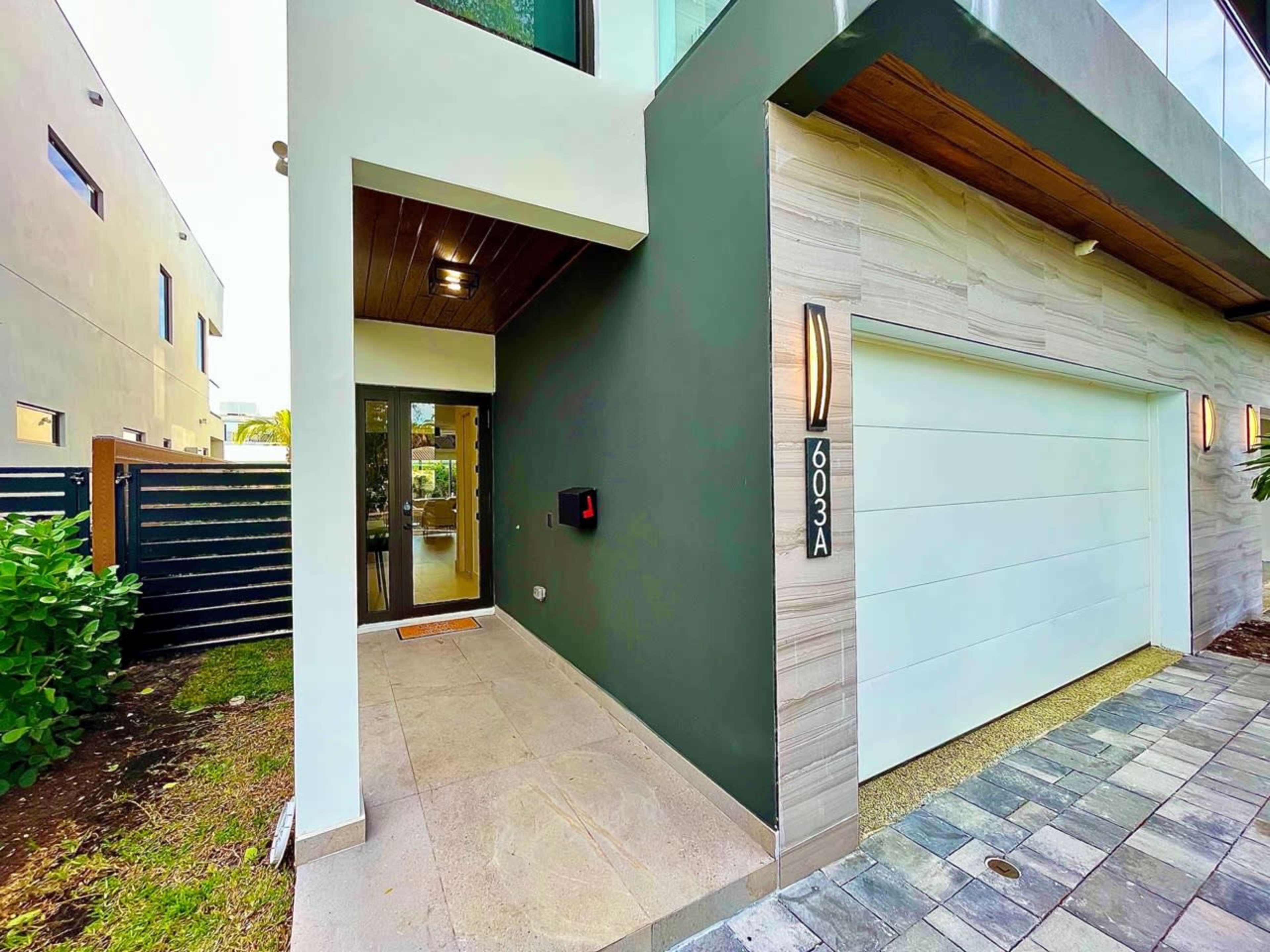 The image shows the entrance of a modern house with a garage and a pathway lined with stone tiles.