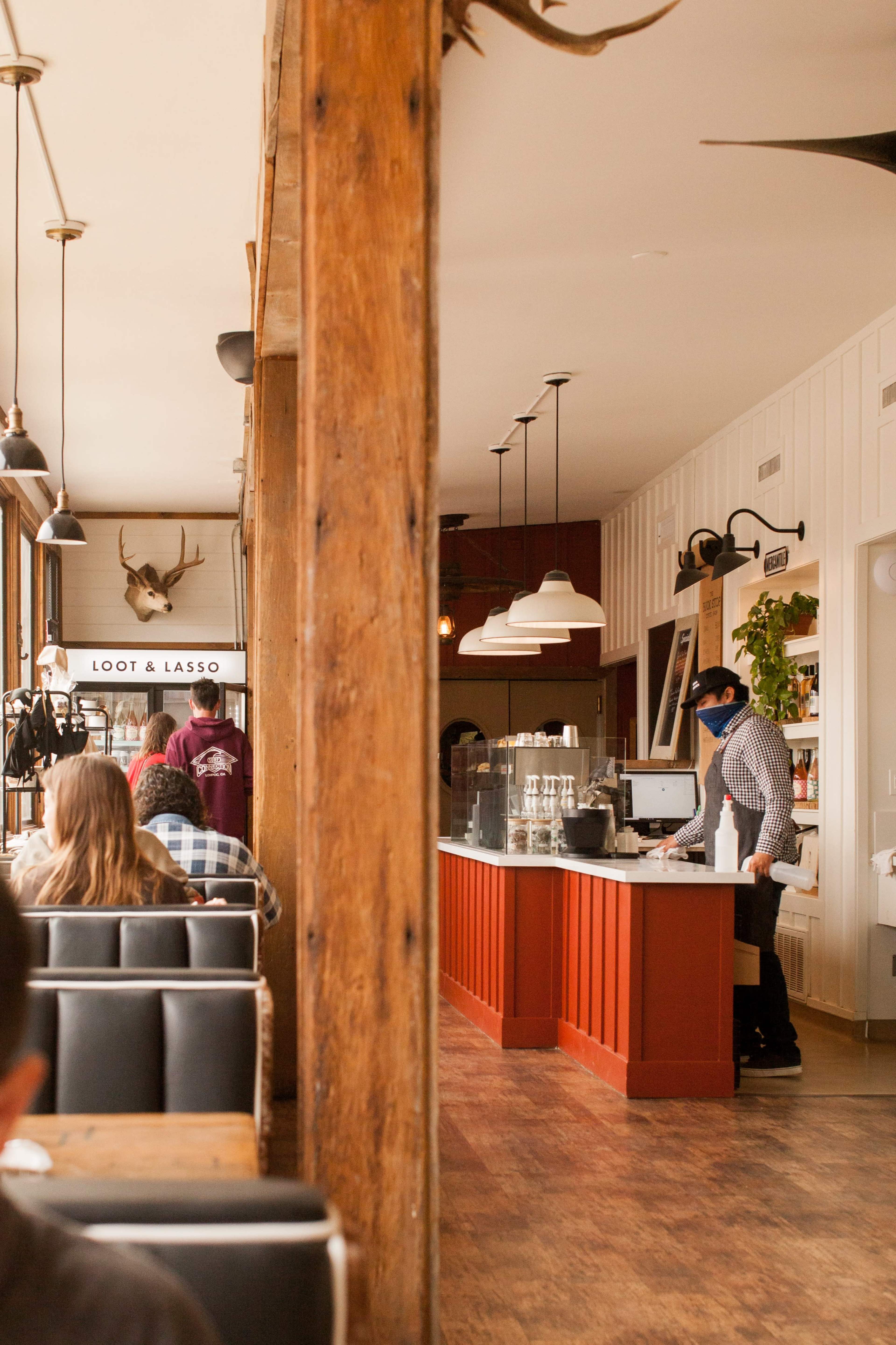 A cozy café interior with wooden beams, a counter where a barista is preparing drinks, and patrons seated at tables in the background.