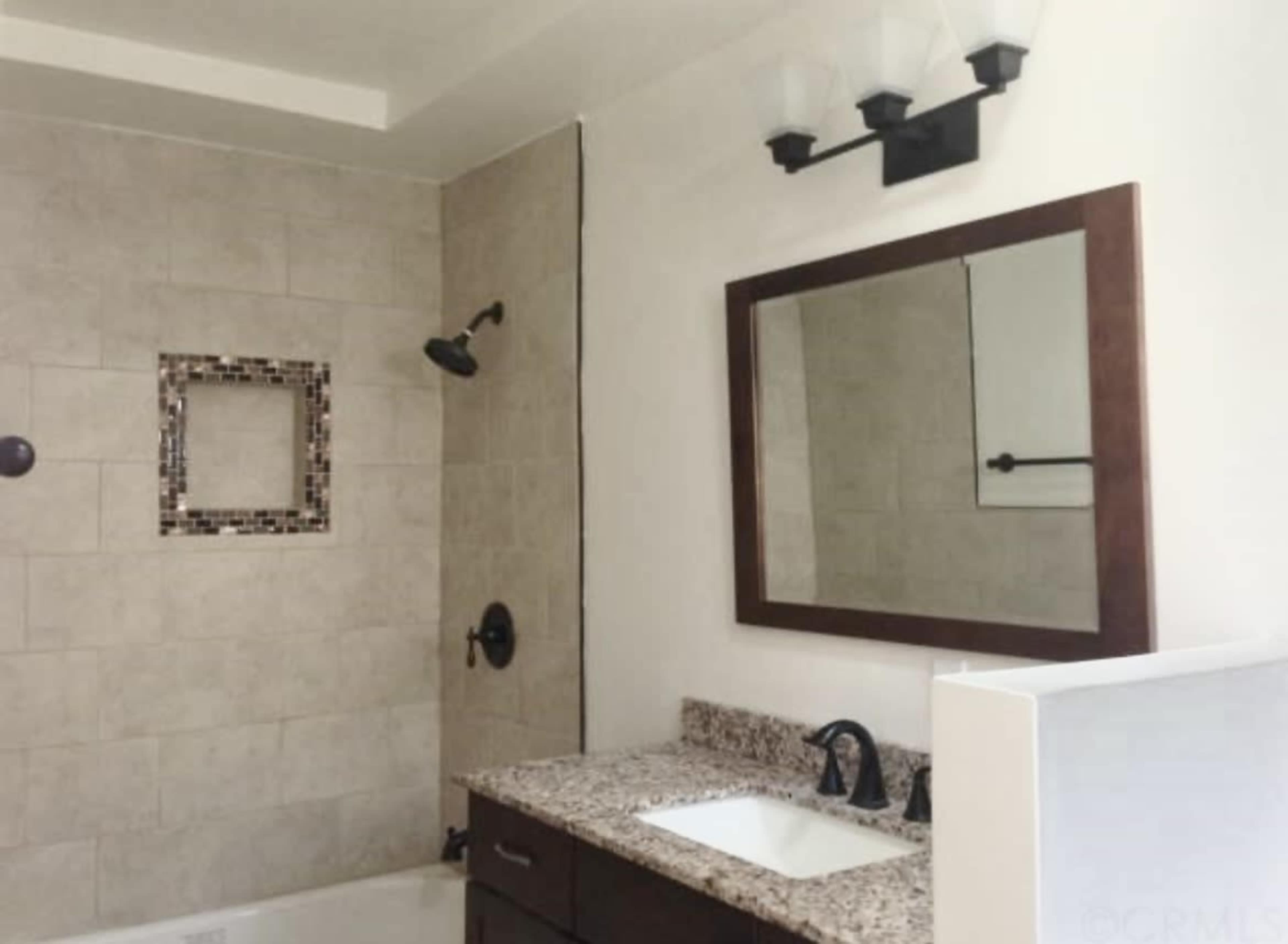 A modern bathroom featuring a tiled shower, a granite countertop sink, and a wall-mounted mirror.