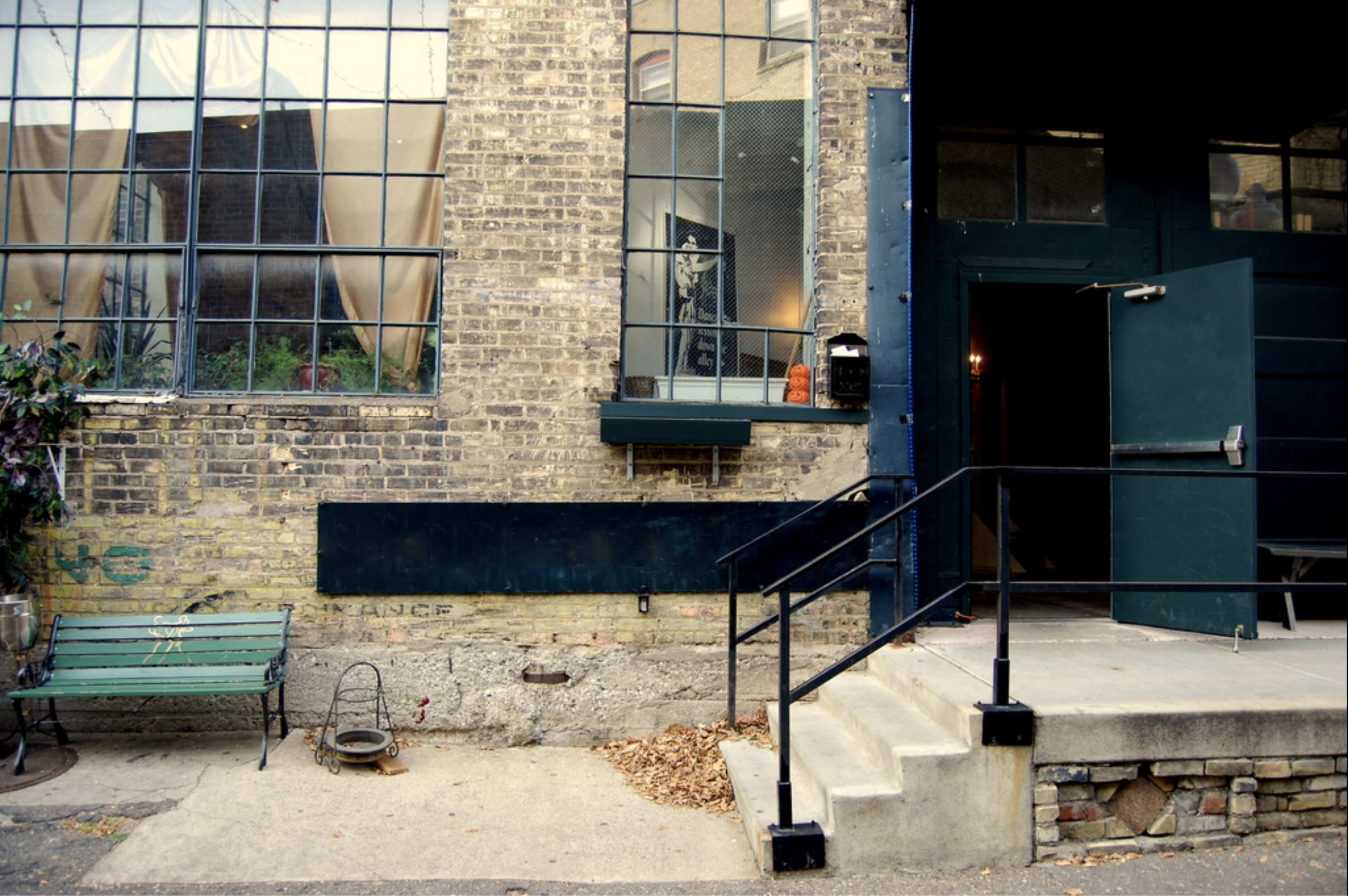 A brick building features large windows, a green bench, and a set of steps leading to a dark green entrance.