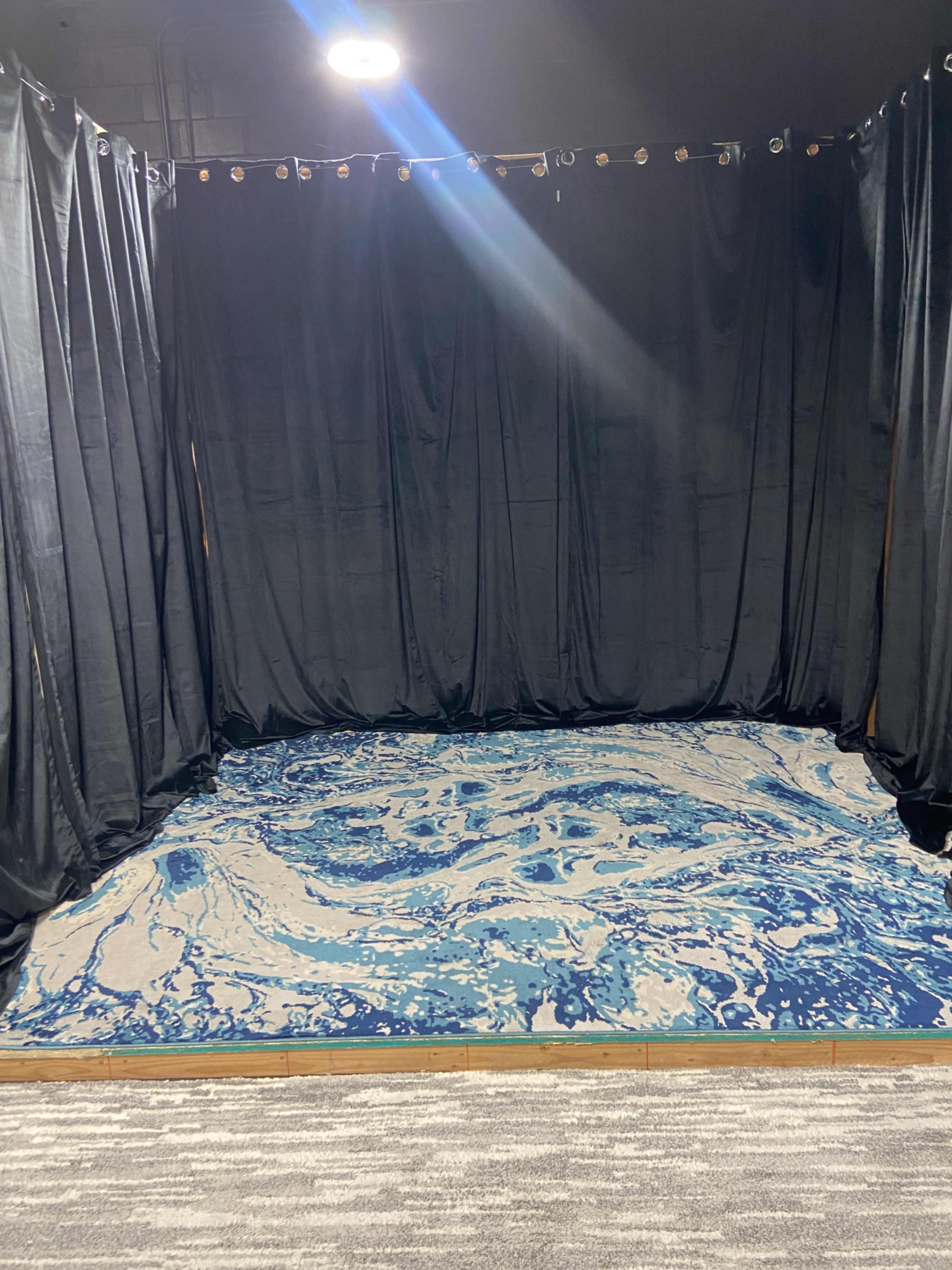 A small, enclosed space with black curtains and a blue patterned rug on the floor.