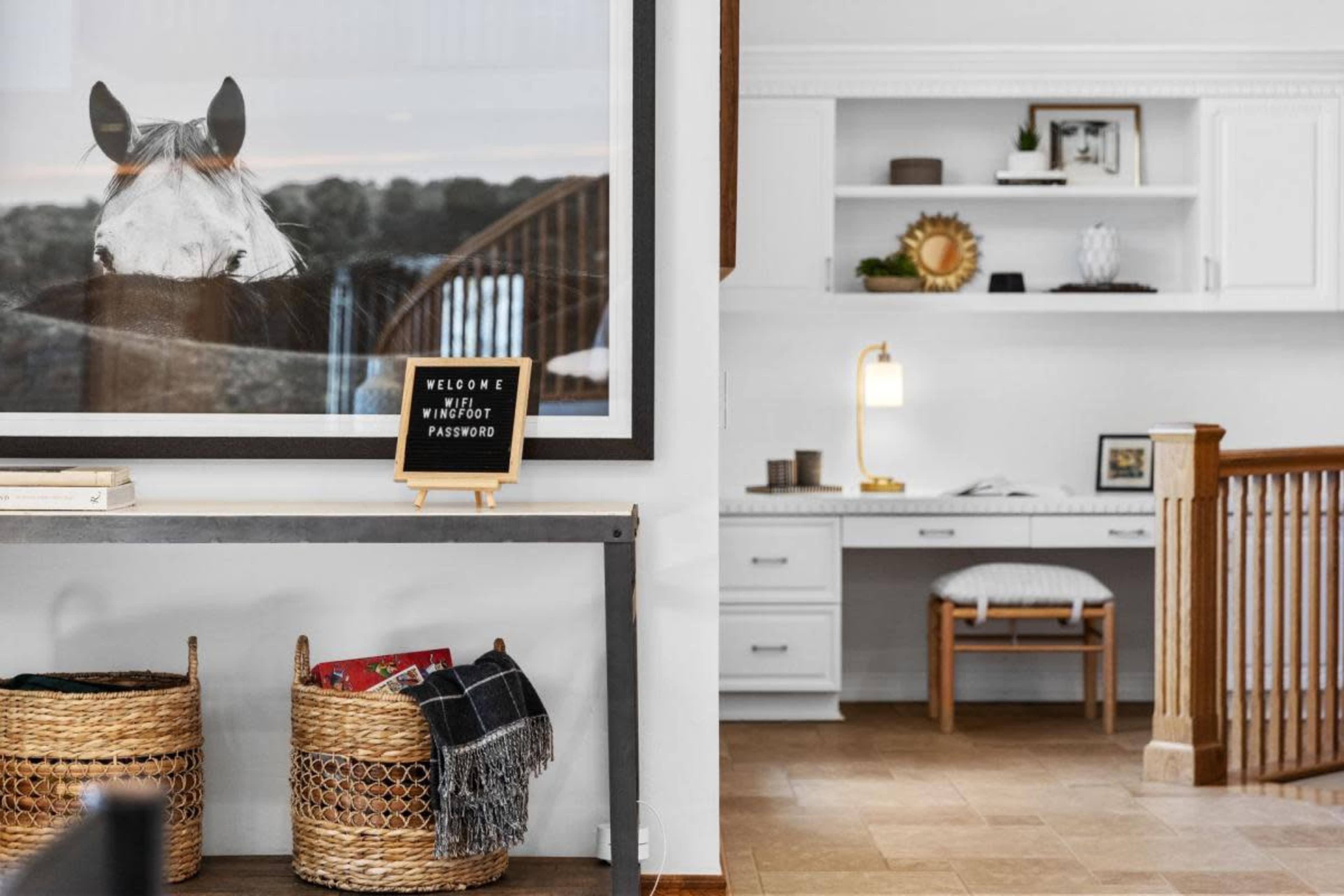 A home interior with a decorative framed horse print on the wall and a desk area with a warm lamp and organized shelves.