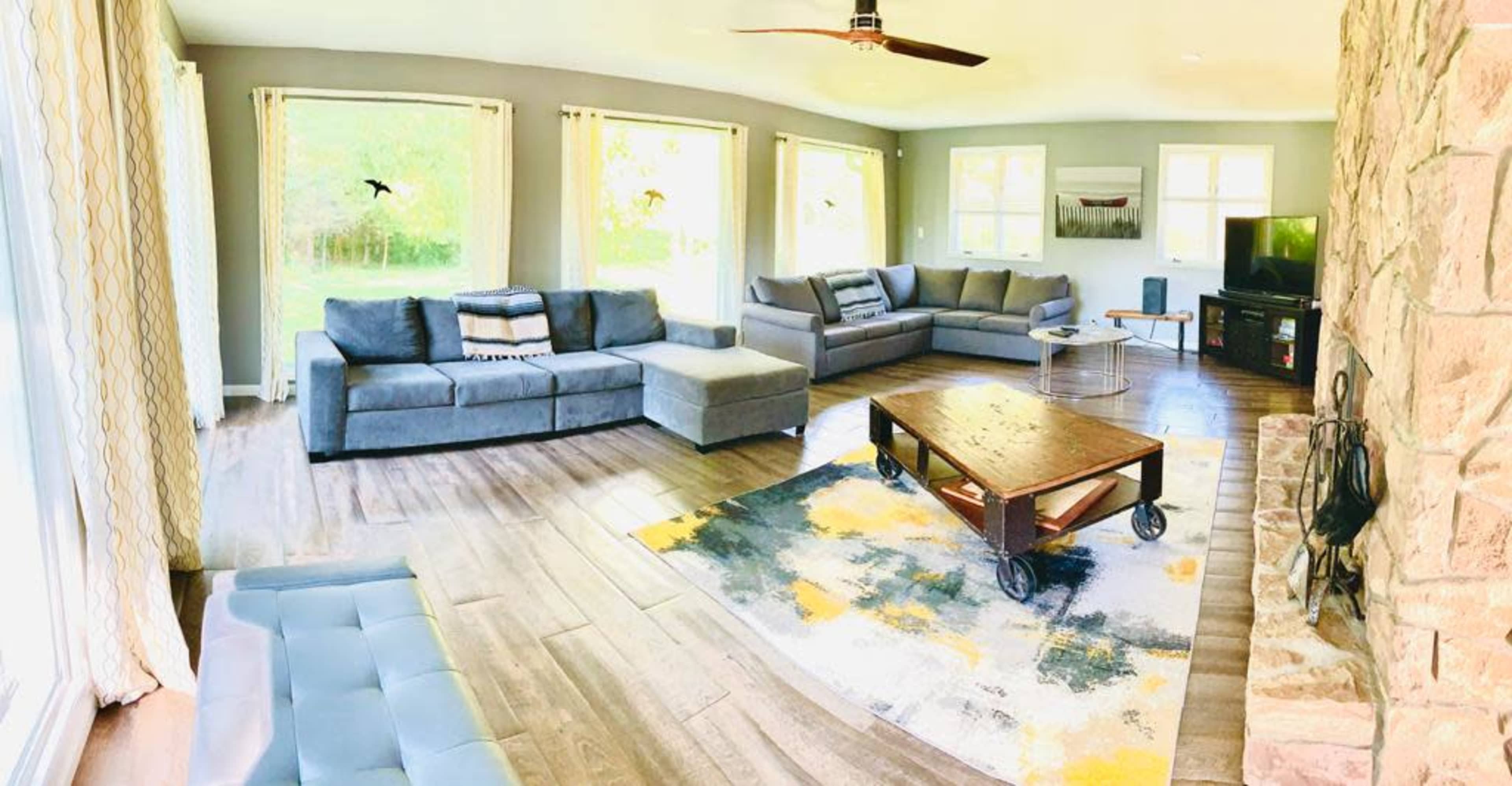 The living room features a sectional sofa, a wooden coffee table on wheels, a stone fireplace, and large windows allowing natural light.