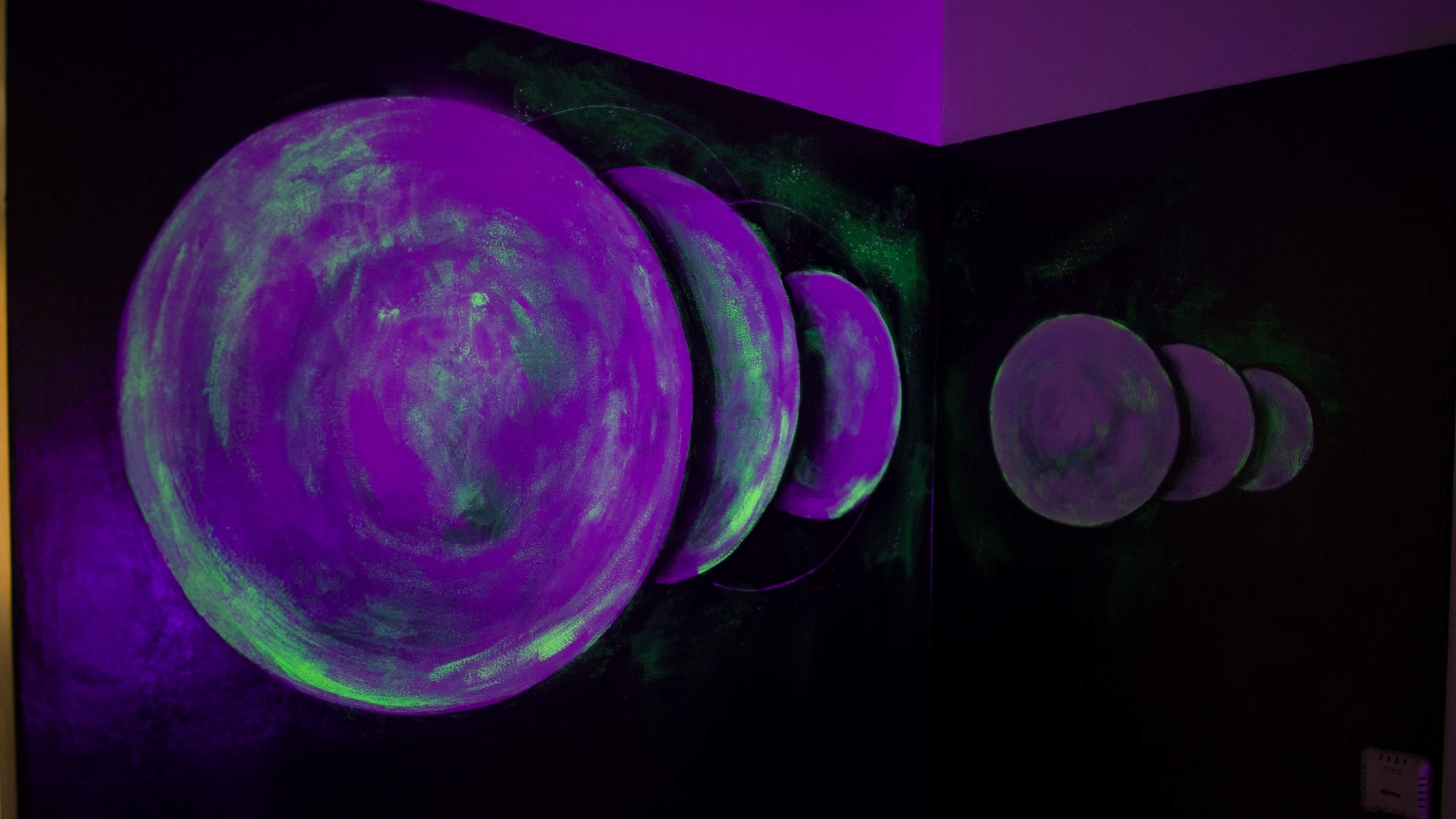 The image shows a wall mural featuring a series of purple and green planets arranged in a gradient along the corner of a dark room.