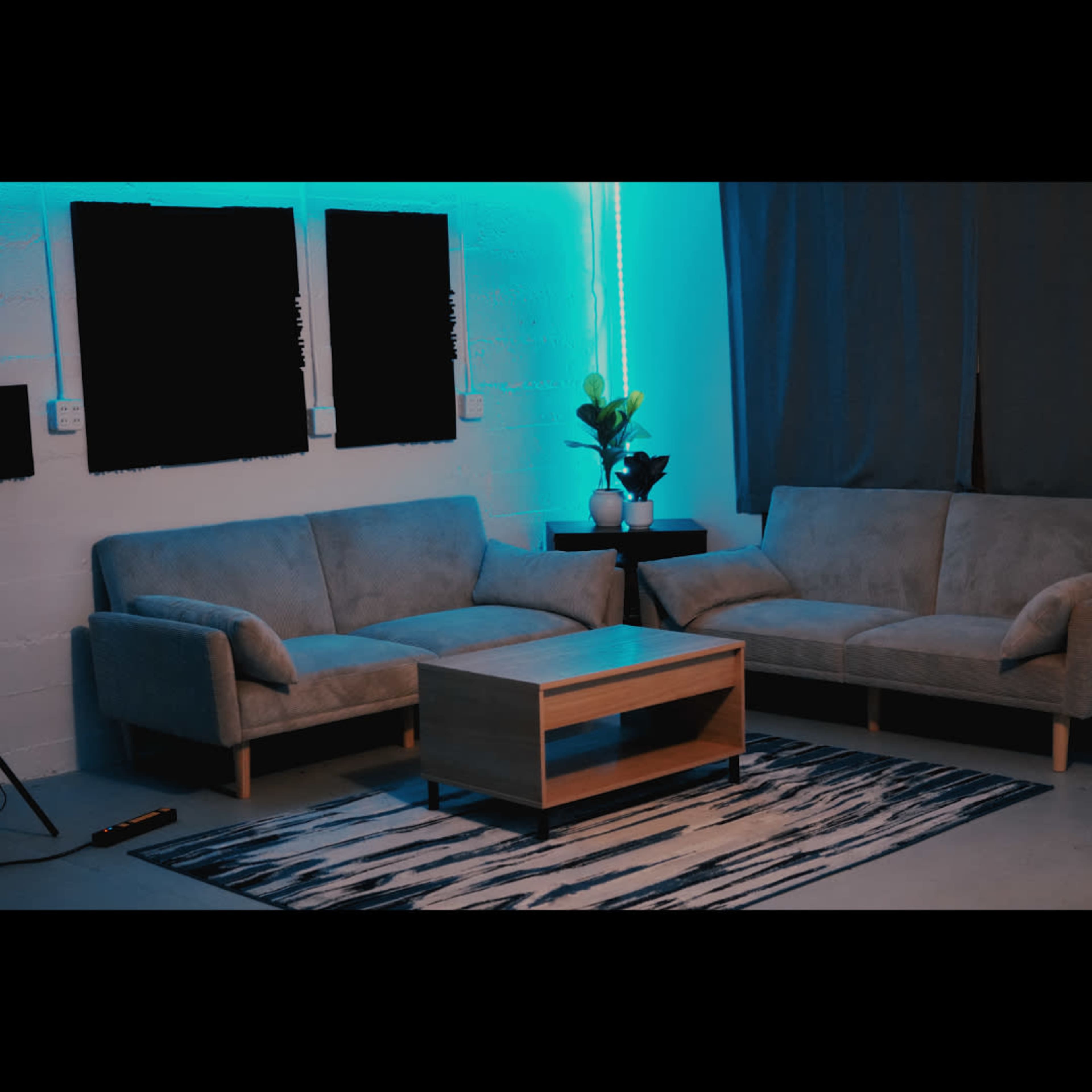The image shows a modern living room setup featuring two light-colored sofas, a wooden coffee table, and a plant on a side table, with blue lighting illuminating the space.