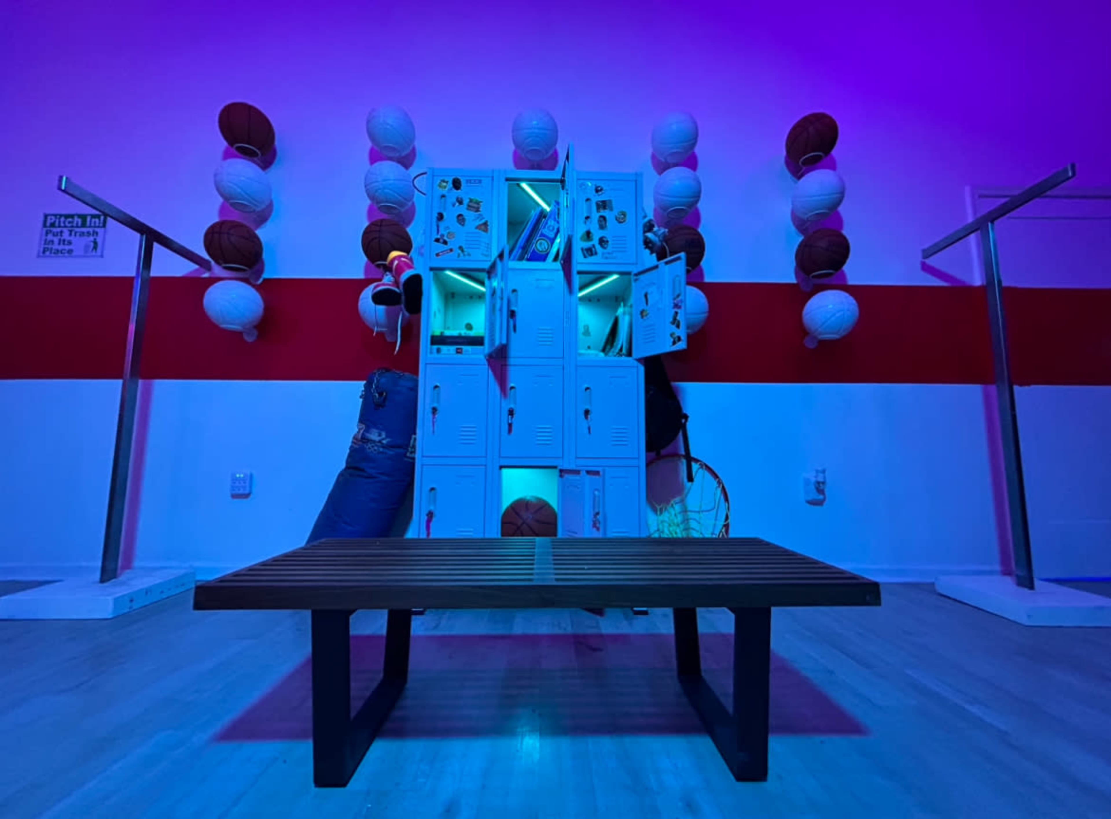 The image features a gym area with colorful lighting, showcasing lockers, basketballs, and a bench in front.