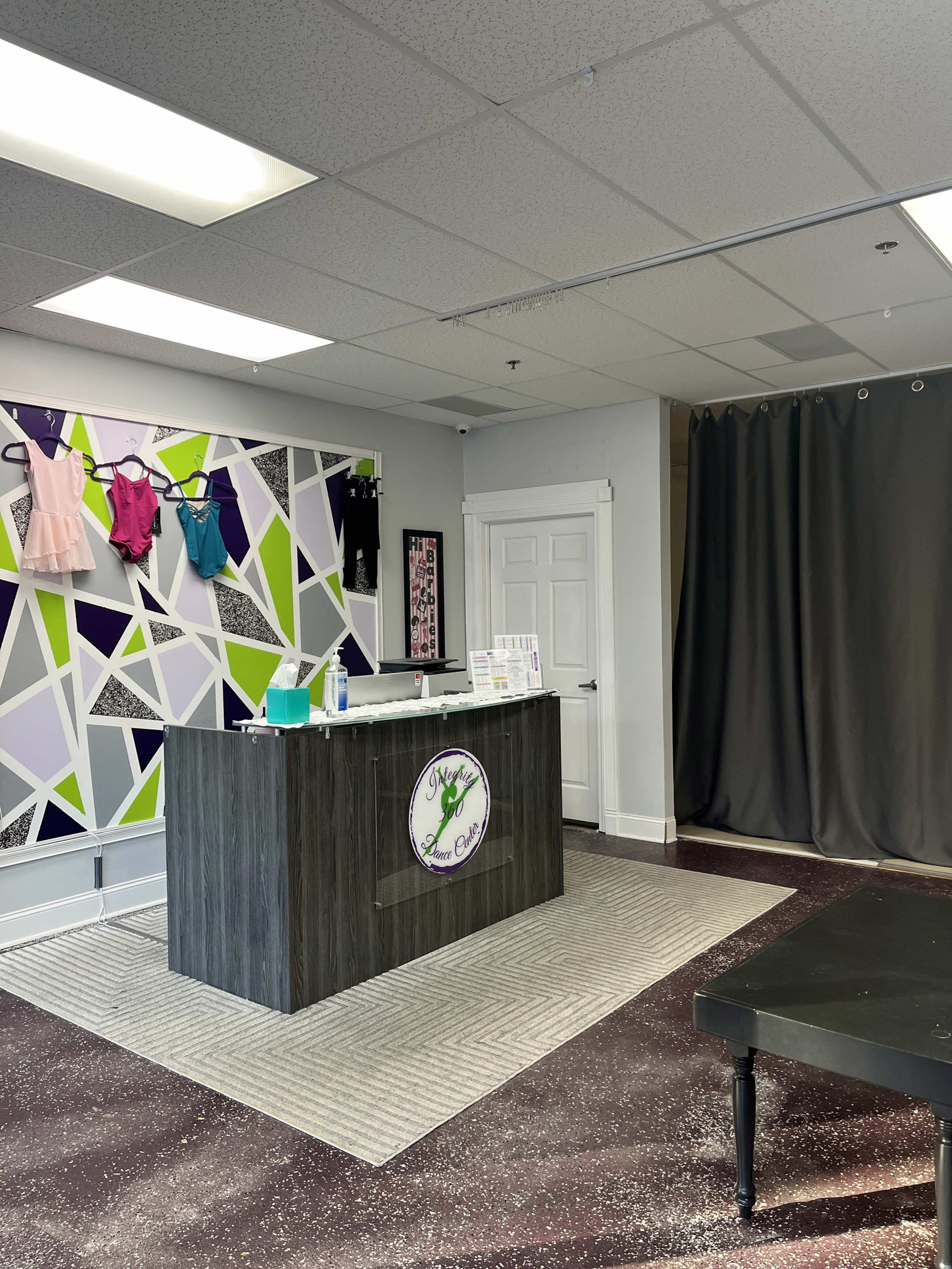 The image shows a reception area with a modern desk, colorful wall displays of apparel, and a fitting room curtain in a boutique setting.