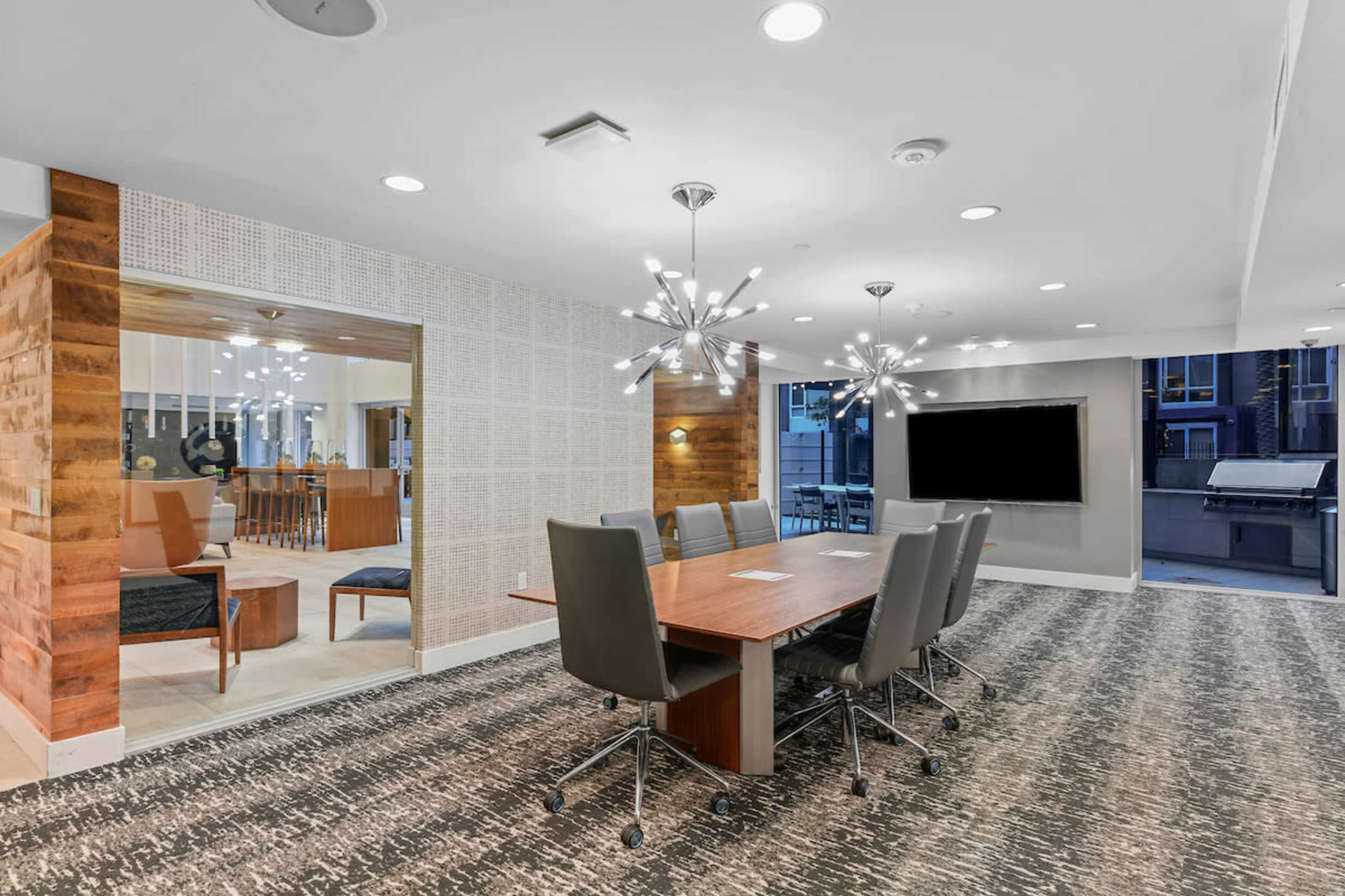 A modern conference room with a large wooden table, padded chairs, and contemporary light fixtures.