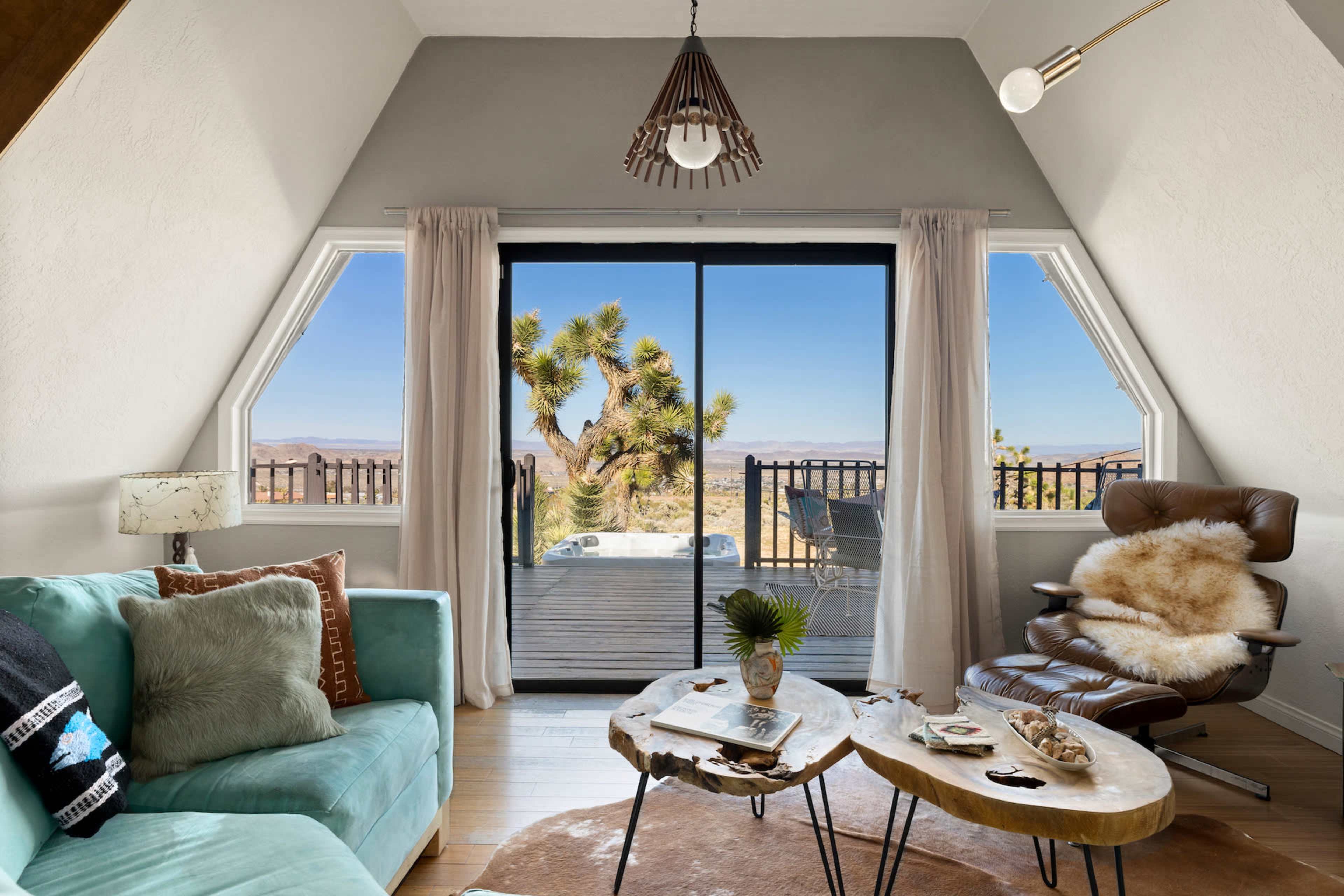 A cozy living area features a teal couch and a wooden coffee table, with large windows offering a view of a desert landscape outside.
