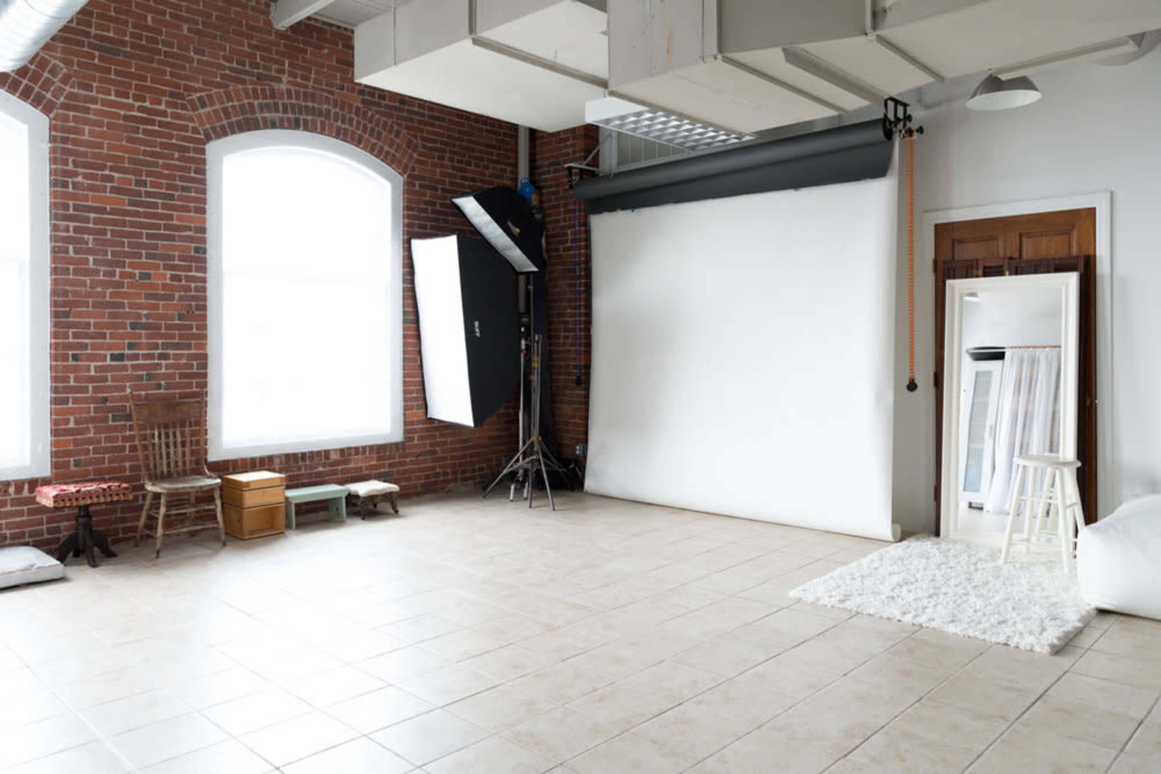 A spacious photography studio features exposed brick walls, a white backdrop, and multiple lighting setups.