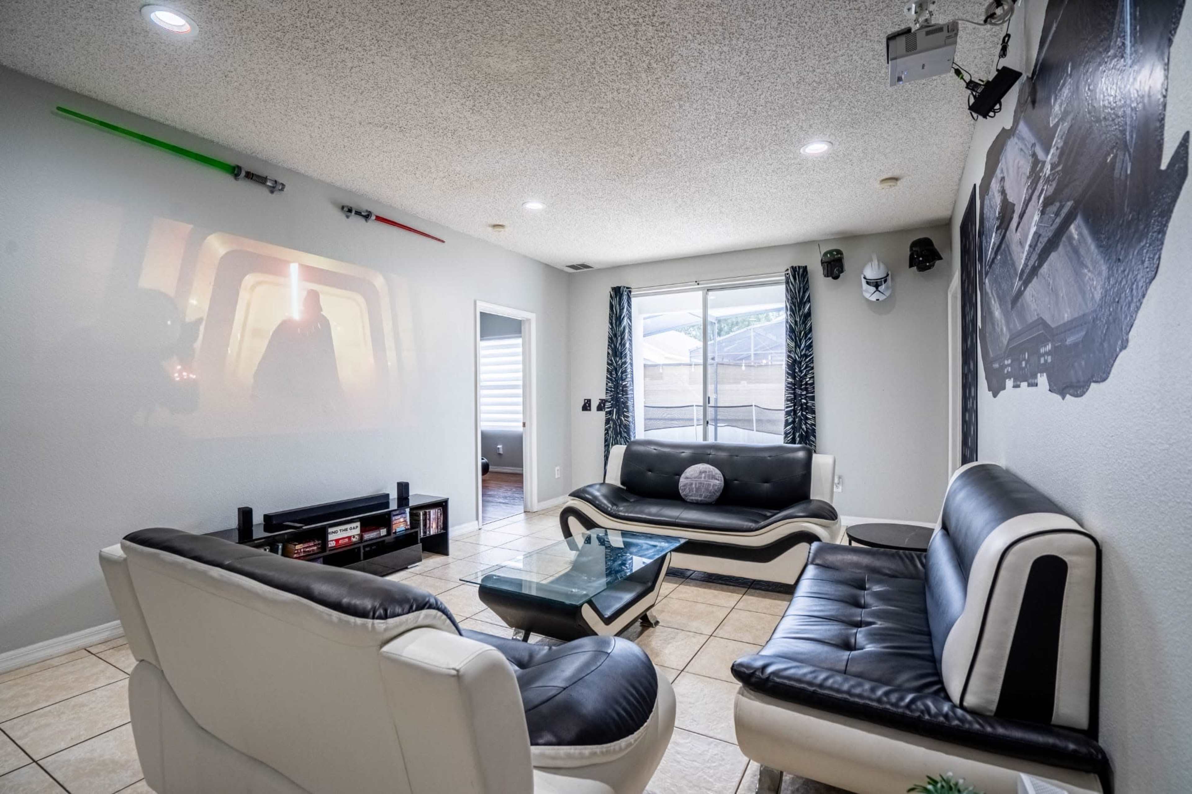A modern living room with a projector displaying a movie scene on one wall, two black and white sofas, and decorative lightsabers mounted on the wall.