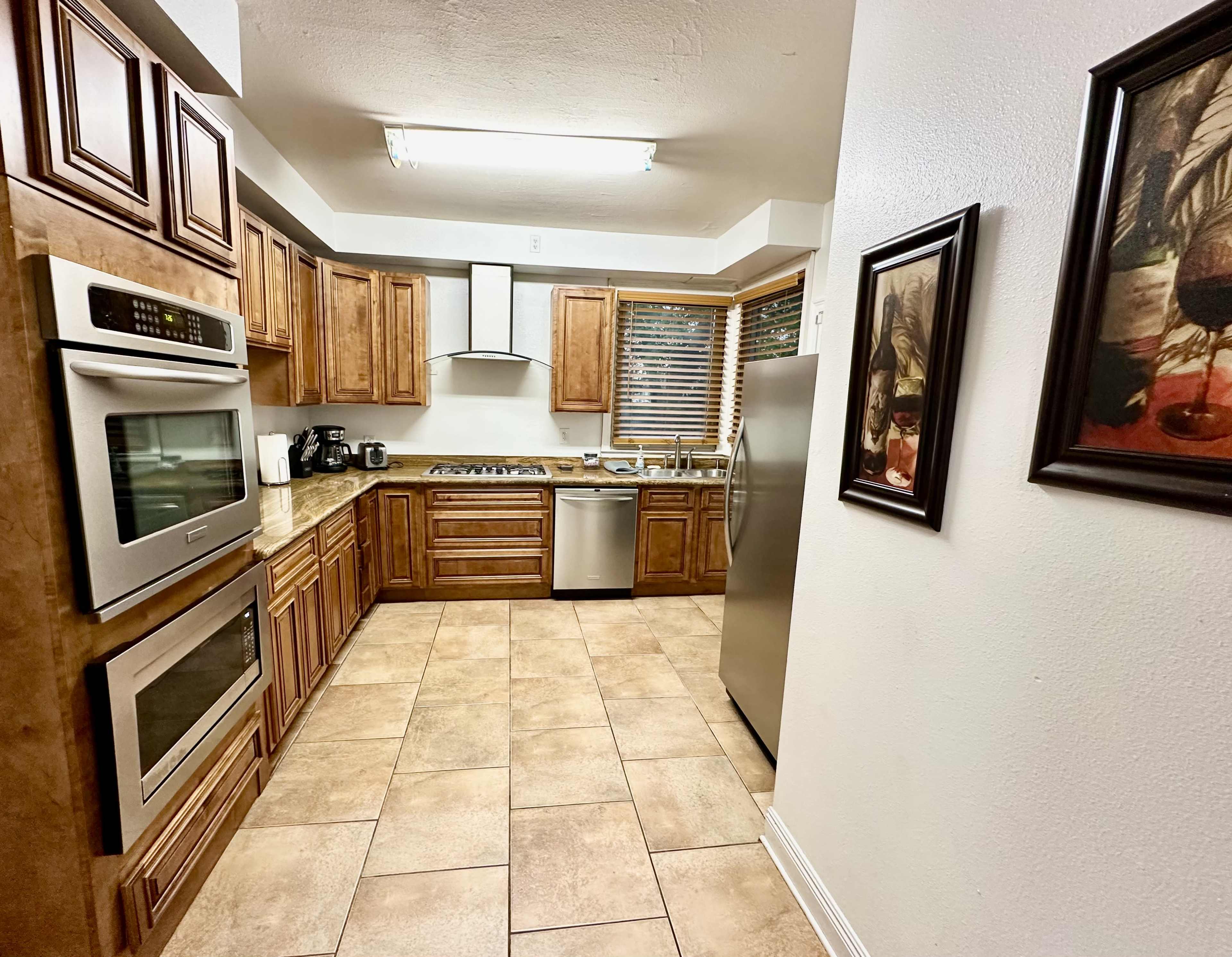 The image shows a kitchen with wooden cabinets, stainless steel appliances, and tile flooring.