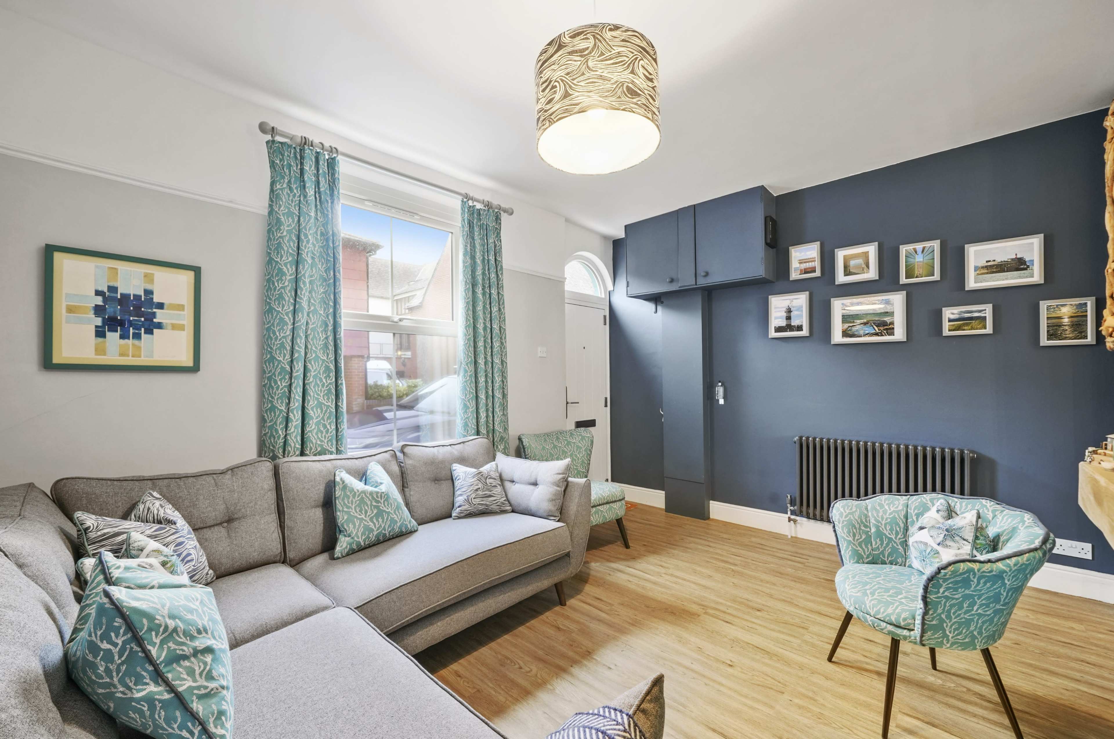 The living room features a gray sectional sofa with decorative cushions, a blue accent wall, and a window letting in natural light.