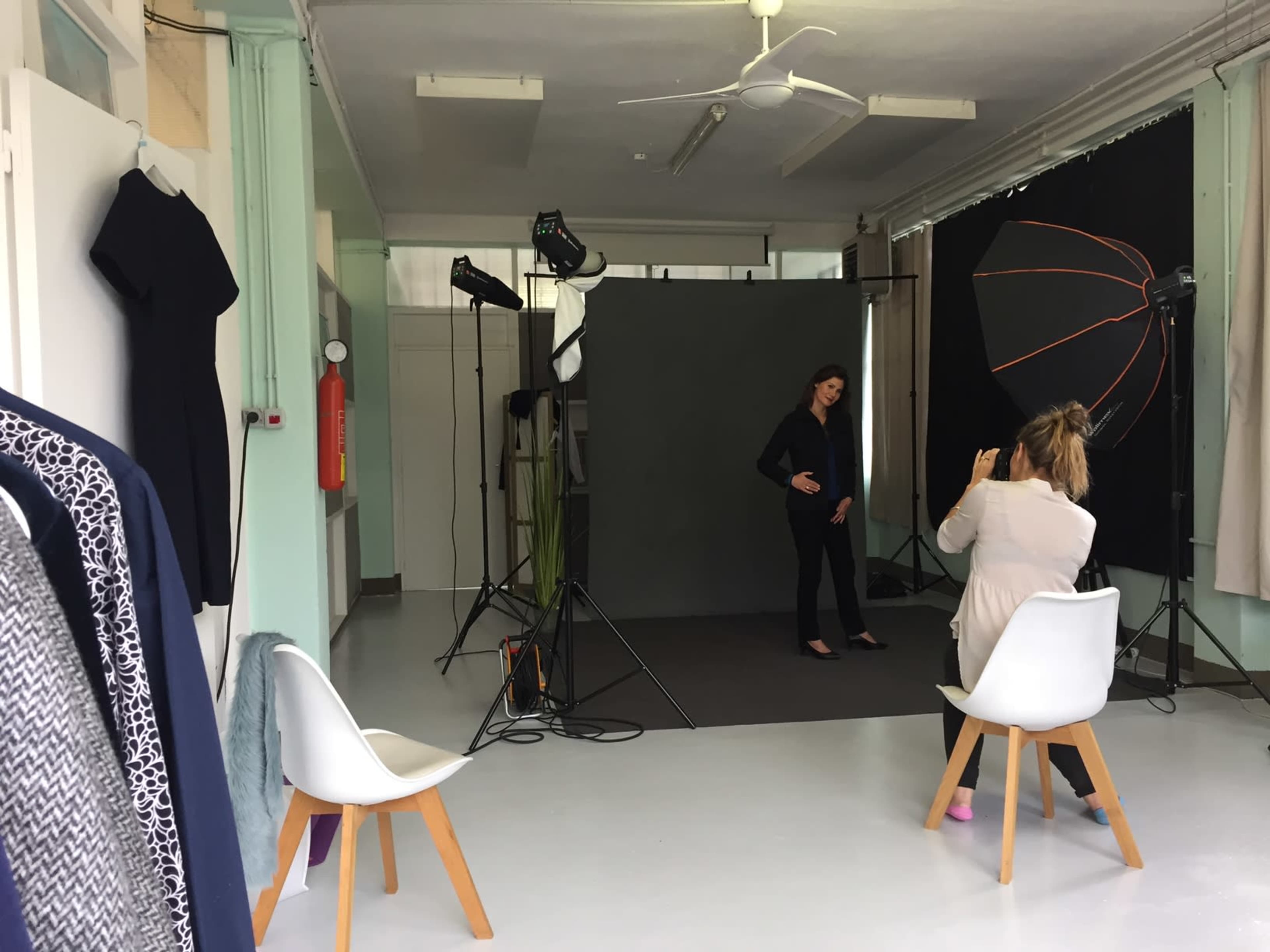 A photographer is capturing images of a model in a studio setting with various lighting equipment and a gray backdrop.