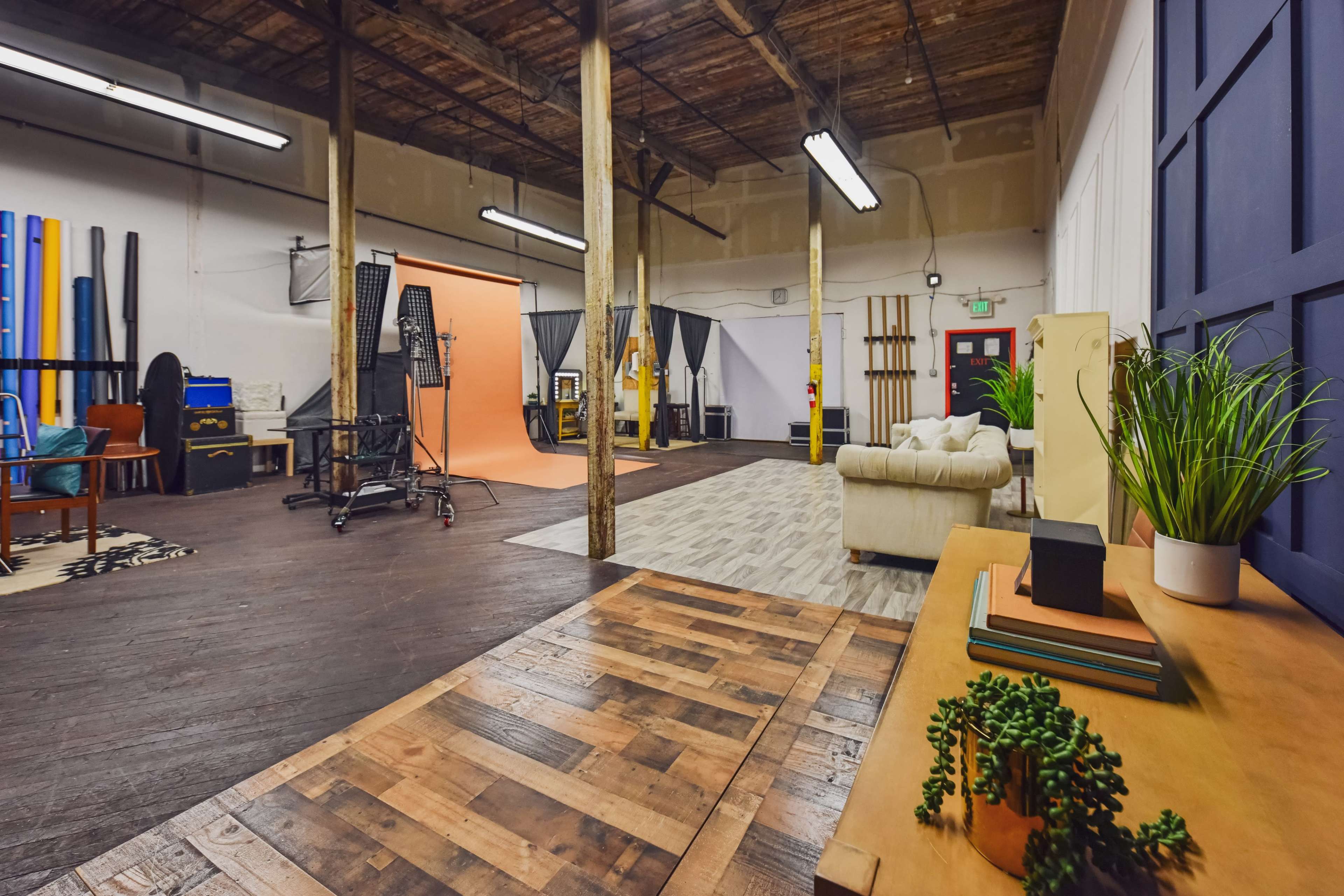 The image shows a spacious photography studio with wooden flooring, a light orange backdrop, and various studio equipment arranged throughout the room.