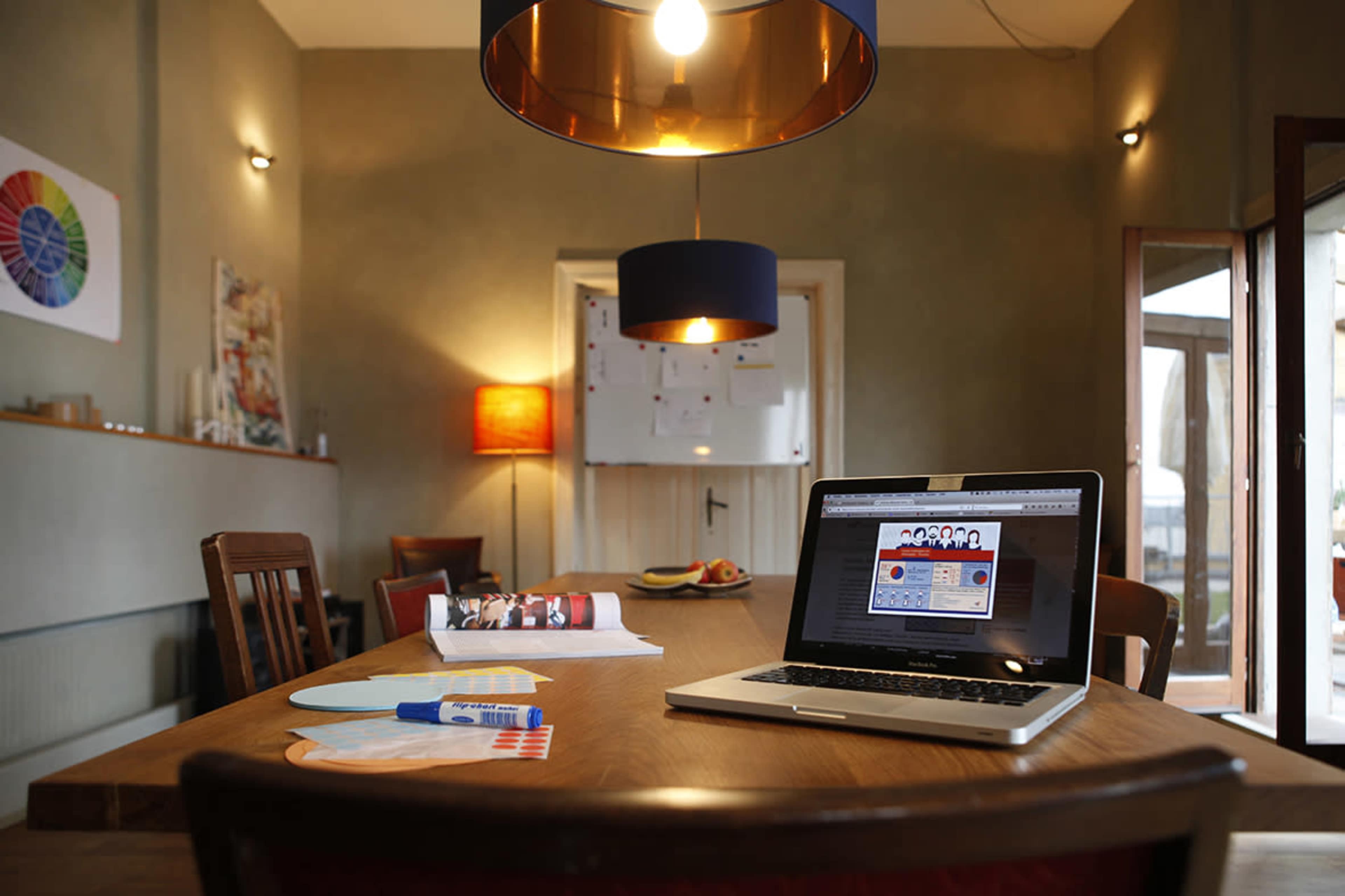 A spacious dining room with a wooden table set up, a laptop open on the table, and various art materials nearby.