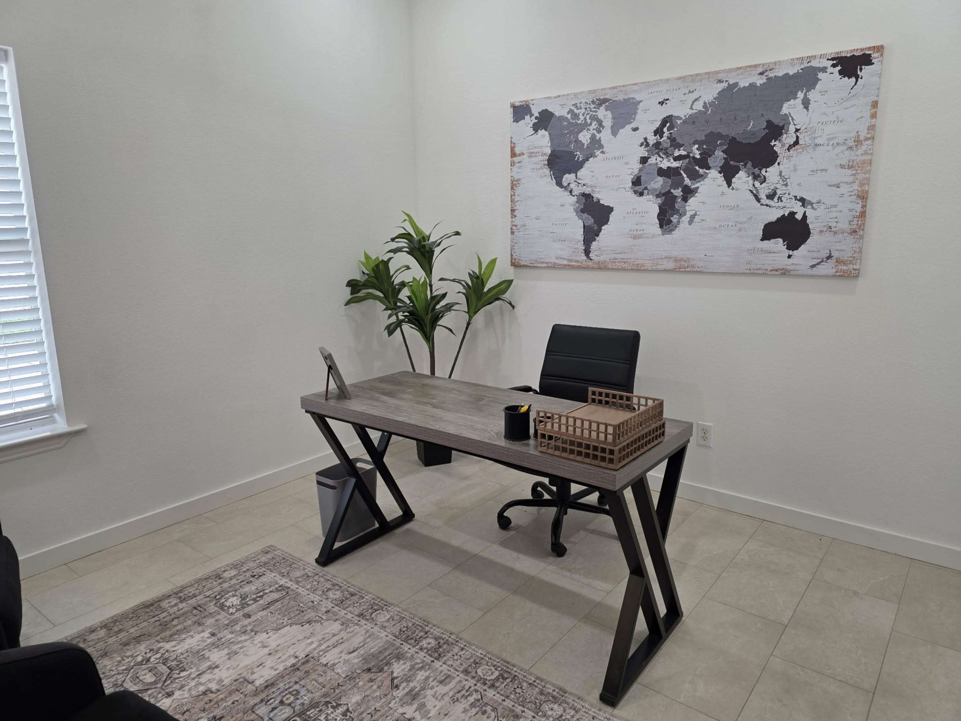 The image depicts a modern office space featuring a sleek desk, an ergonomic chair, a world map on the wall, a potted plant, and a neutral-colored rug on the tiled floor.