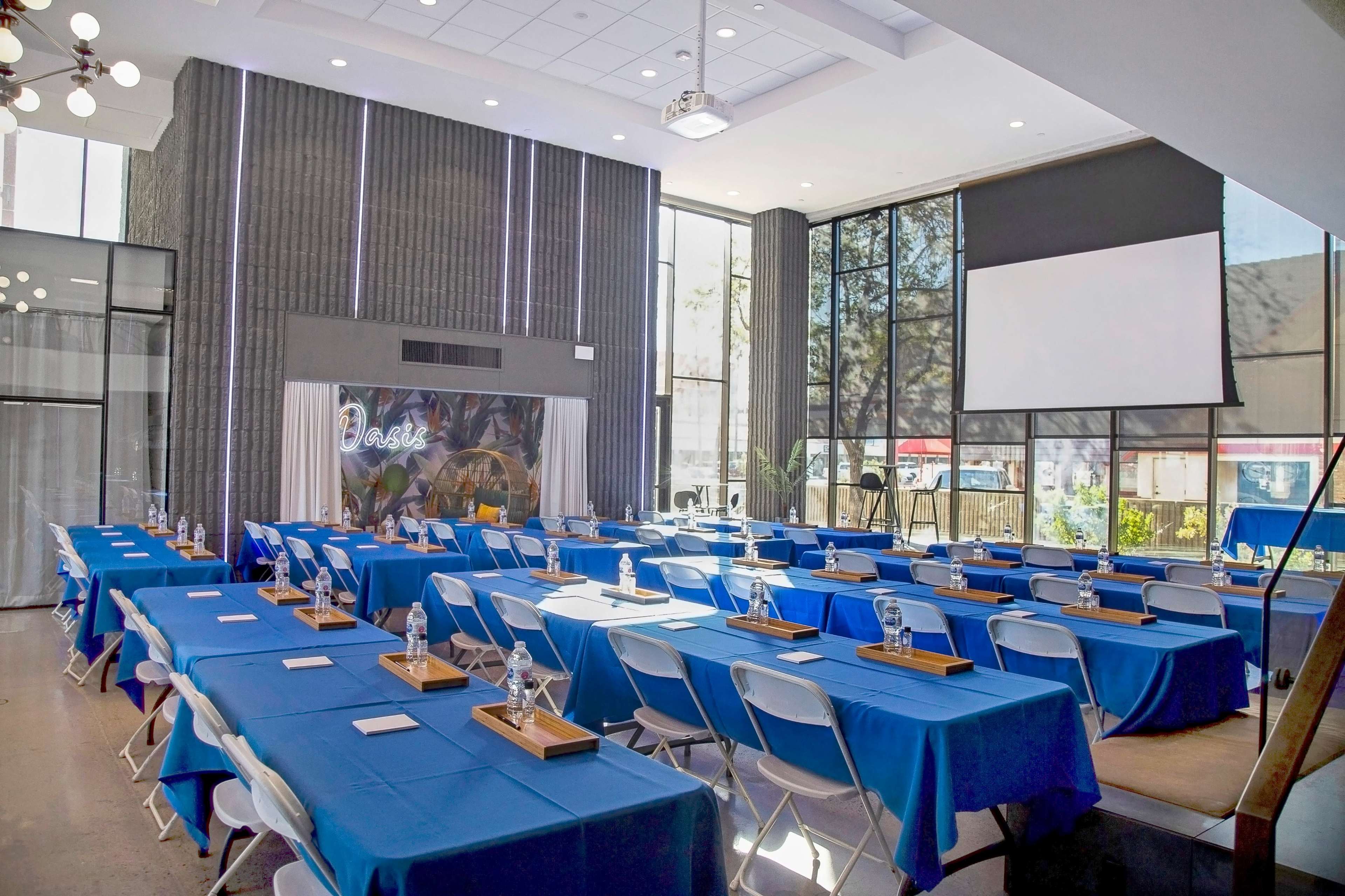 A conference room set up with multiple tables covered in blue cloths, arranged in a rectangular layout, and filled with water pitchers and notepads.