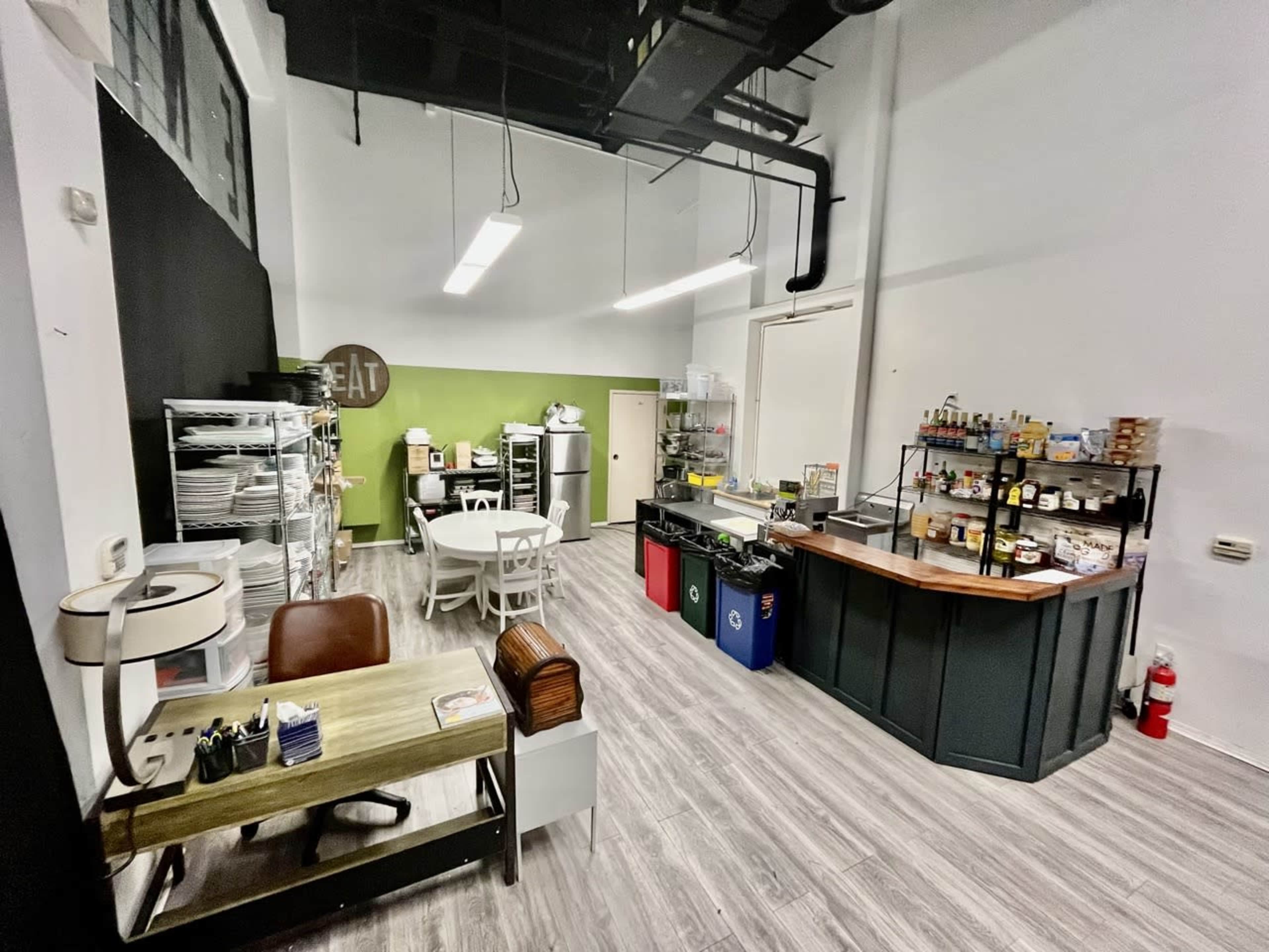 A spacious commercial kitchen area featuring a seating table, workstations, storage shelves, and a service counter.