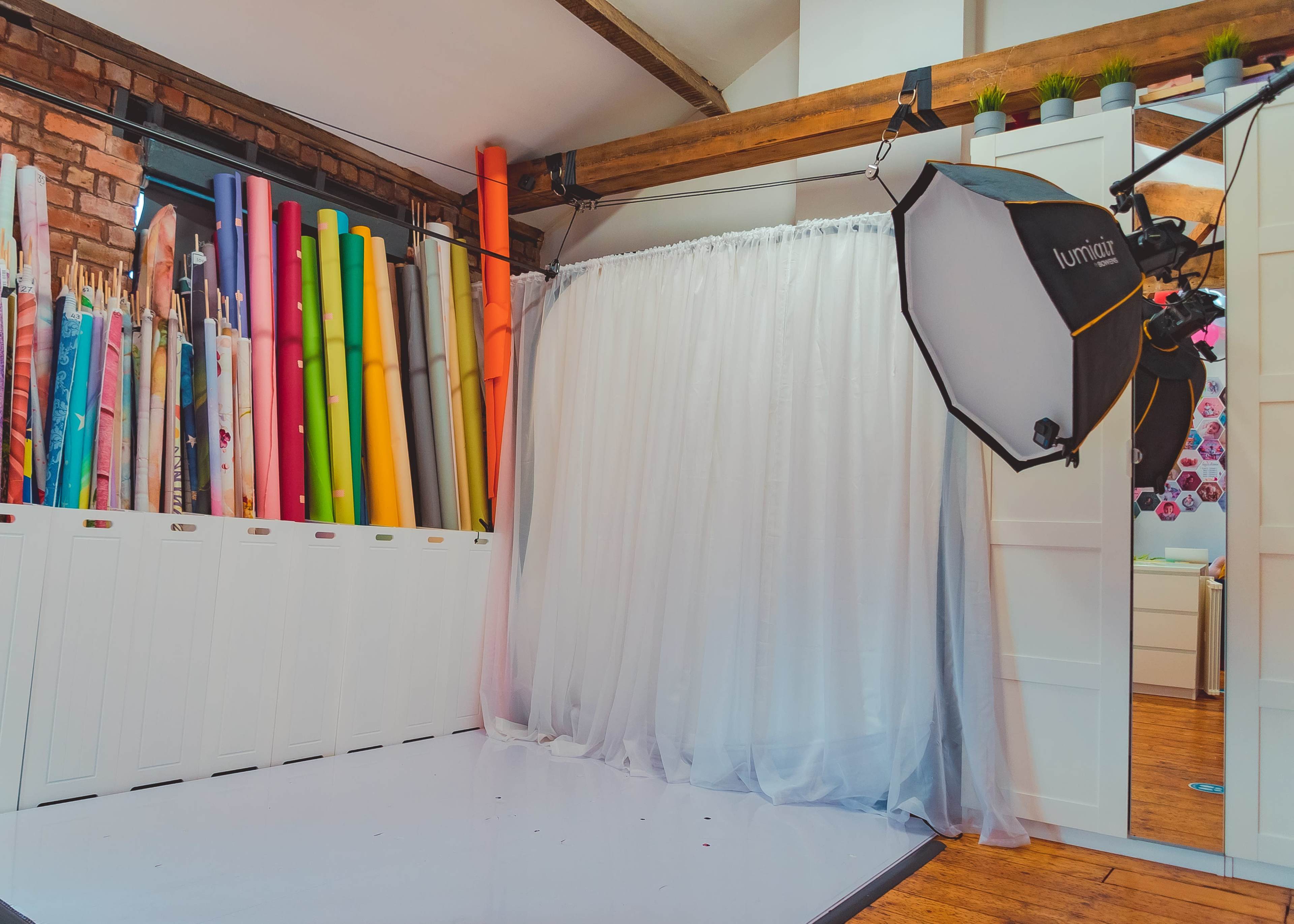 A photography studio featuring a curtain backdrop, lighting equipment, and an array of colored paper rolls displayed against a wall.