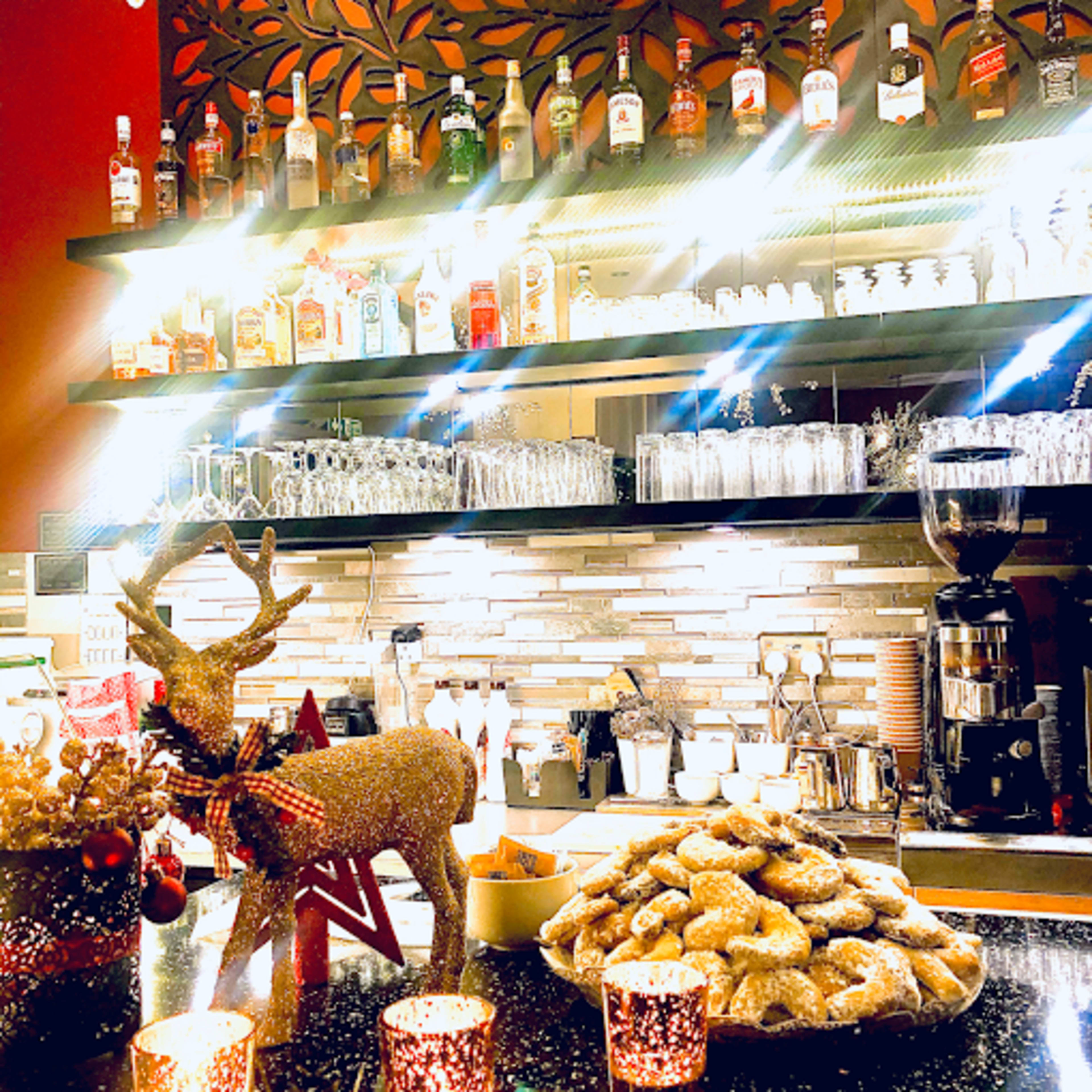 A festive bar with a variety of liquor bottles arranged on shelves, a decorative reindeer, a plate of cookies, and glowing candles on the counter.