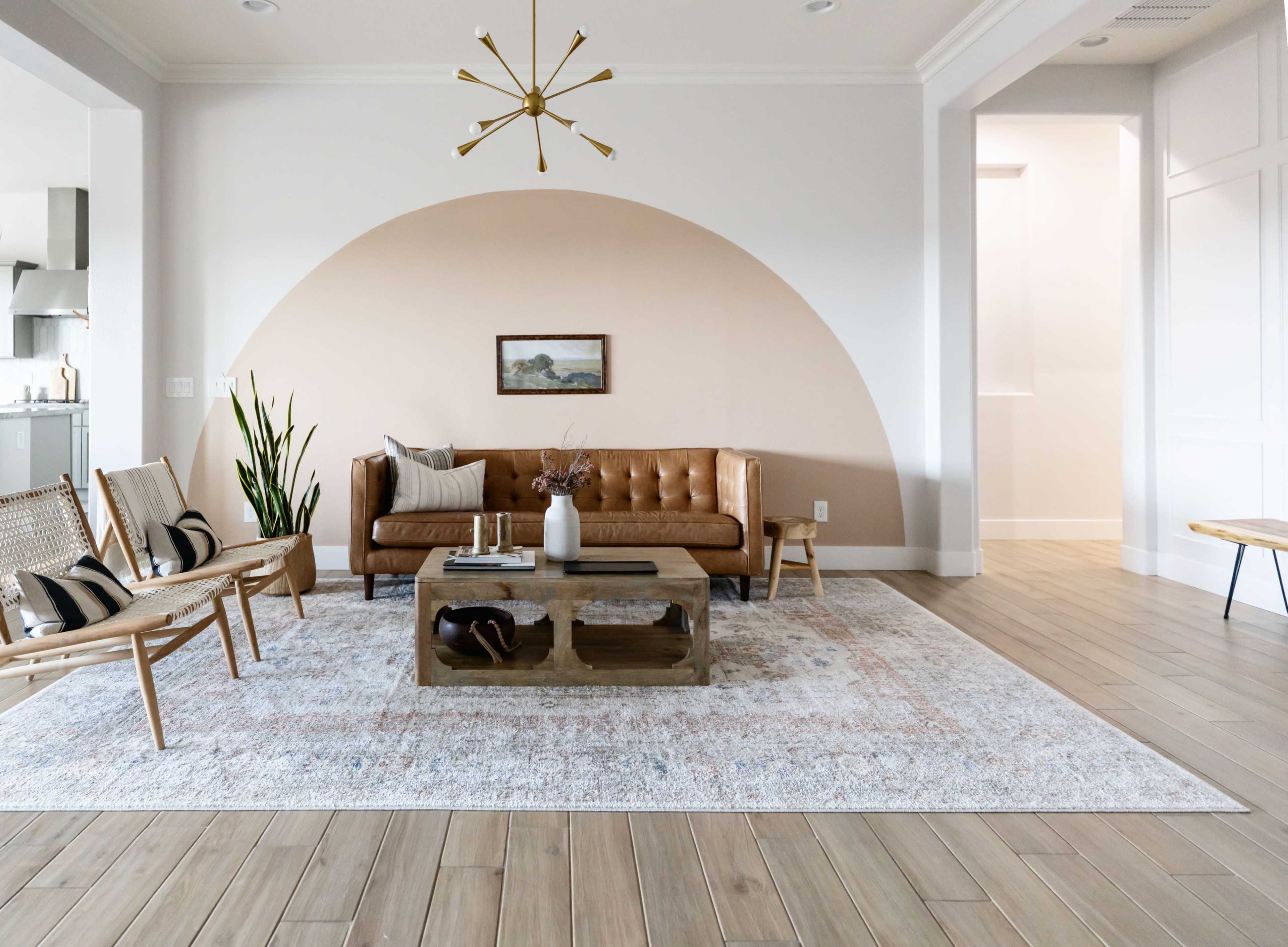The room features a minimalist design with a brown leather sofa, a wooden coffee table, and light-colored walls, highlighted by a curved accent behind the couch.