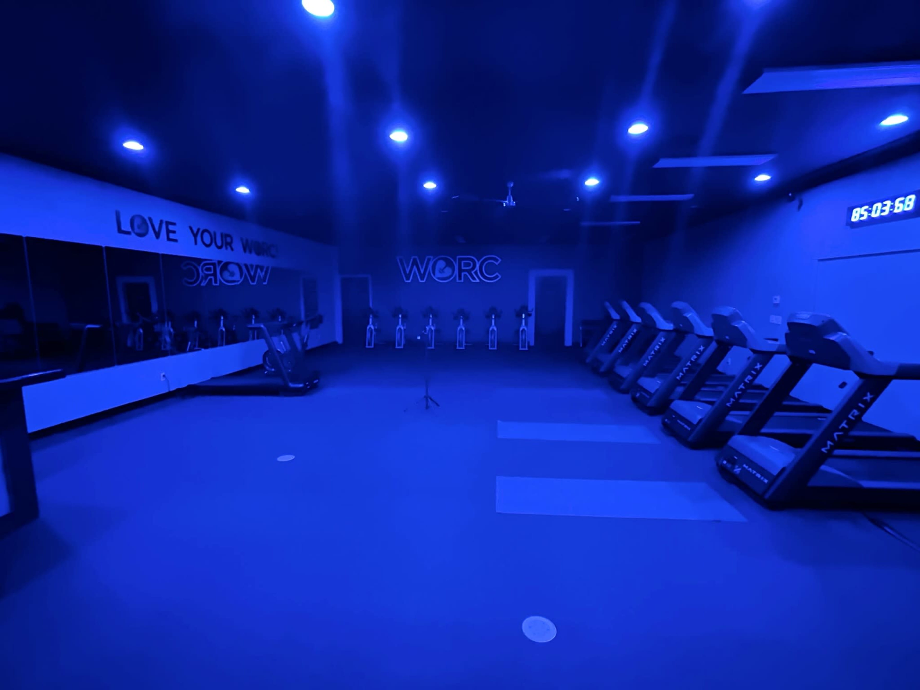A dimly lit gym features a row of treadmills against a wall with motivational phrases and a clock displaying the time.