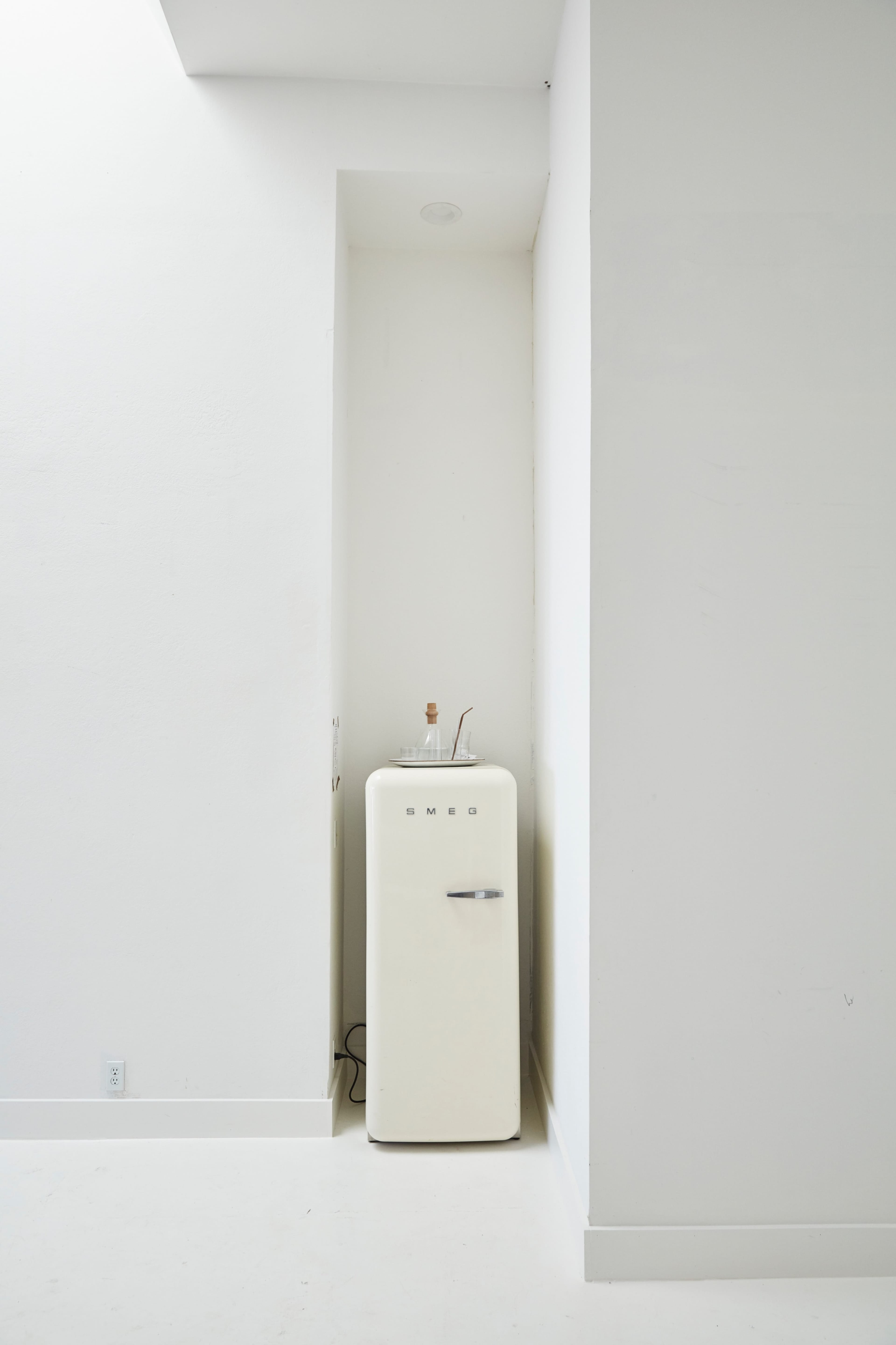 A vintage-style cream-colored refrigerator is positioned in a corner of a bright, minimalist interior.