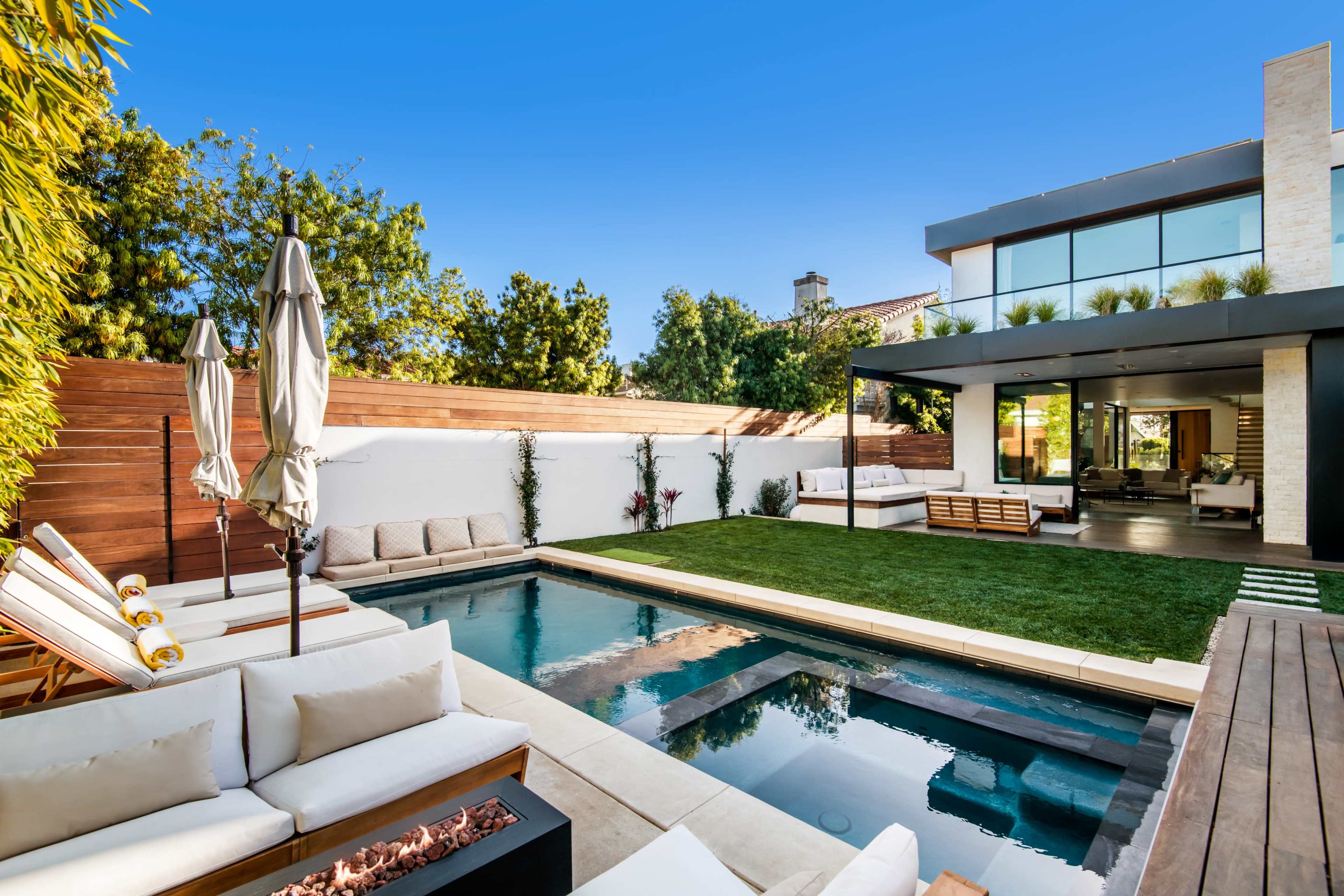 A modern backyard features a pool surrounded by lounge chairs, a grassy area, and a sleek outdoor living space.