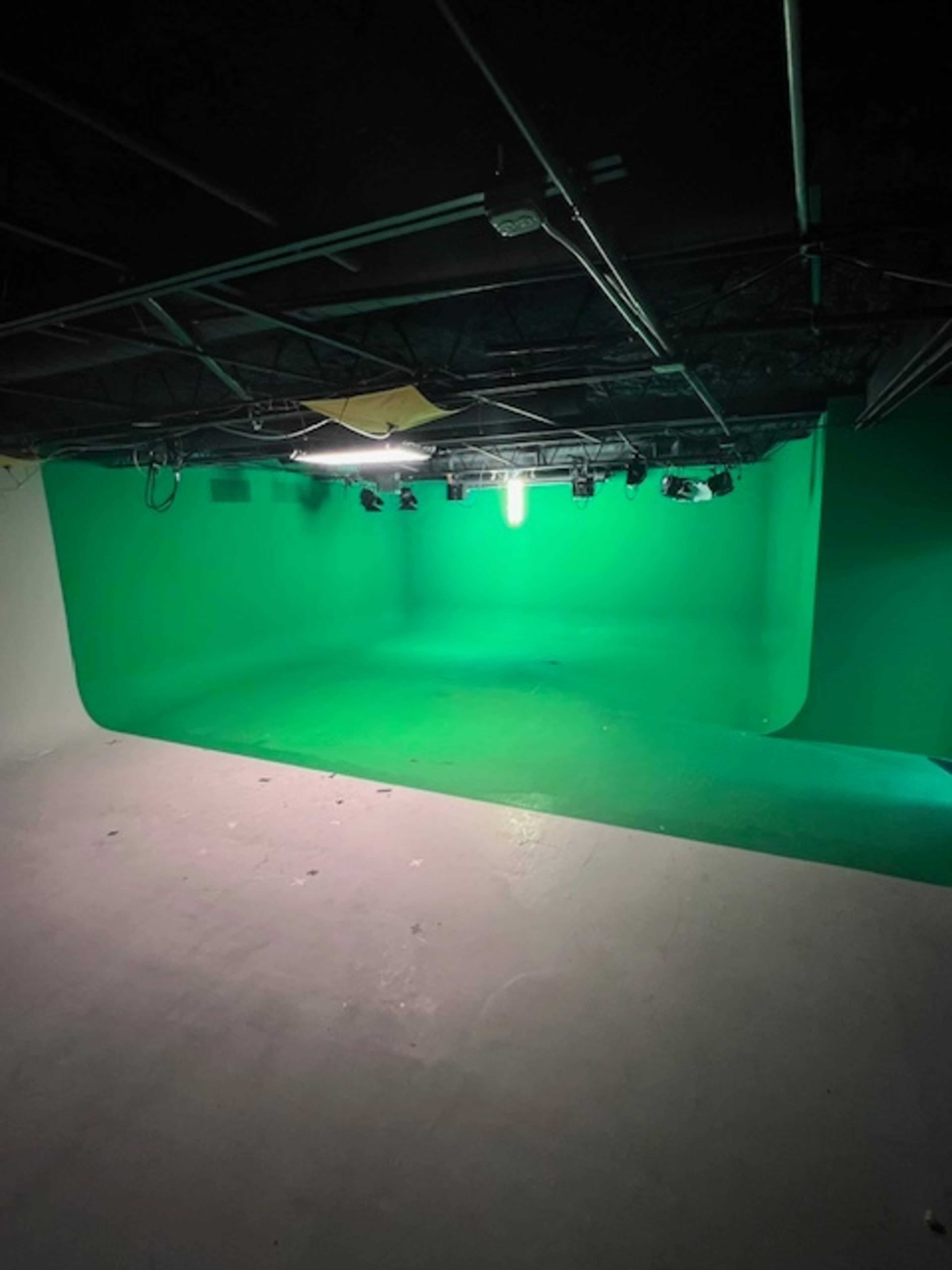 An empty studio with a green screen backdrop and overhead lighting.