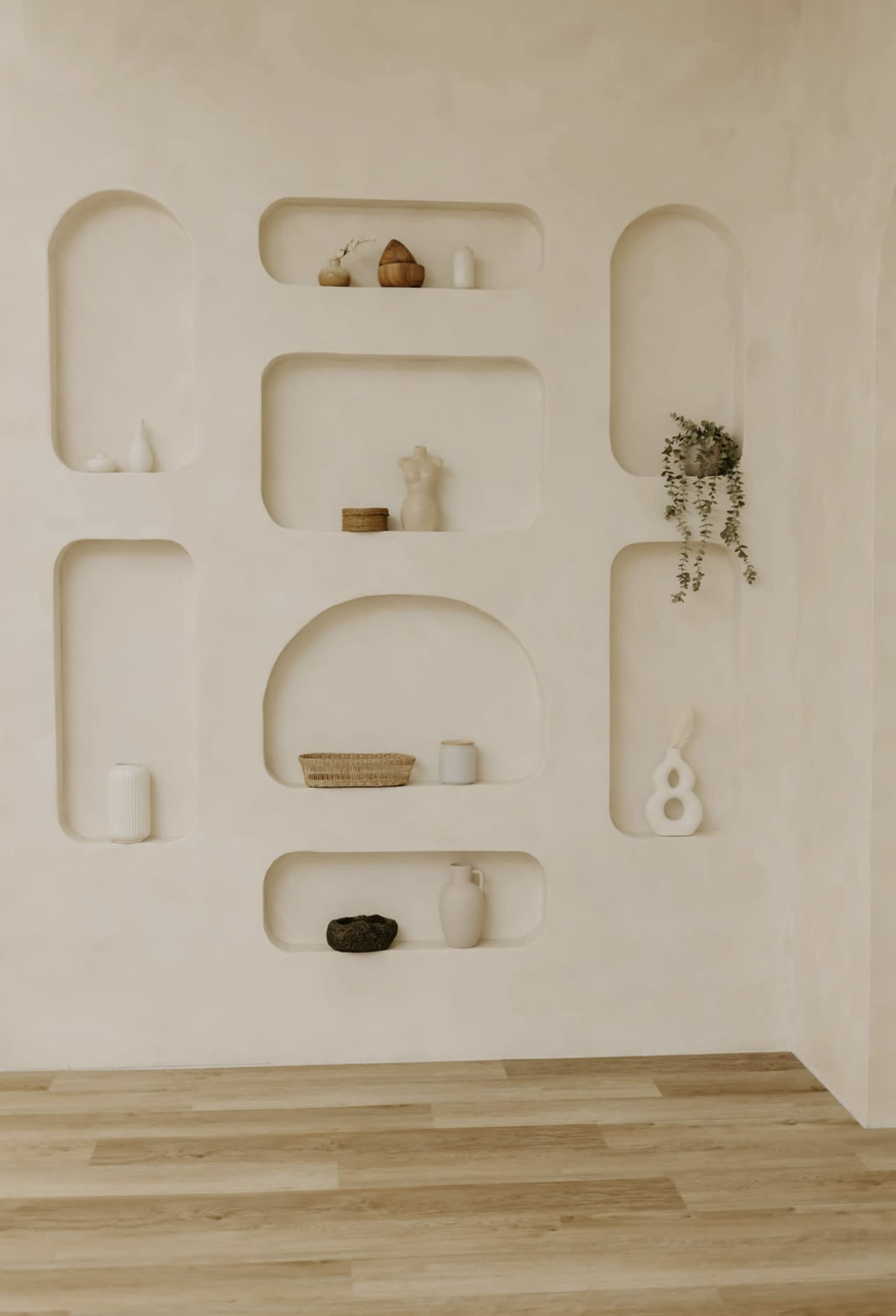 The image shows a textured beige wall with several recessed shelves displaying various decorative items and a plant.