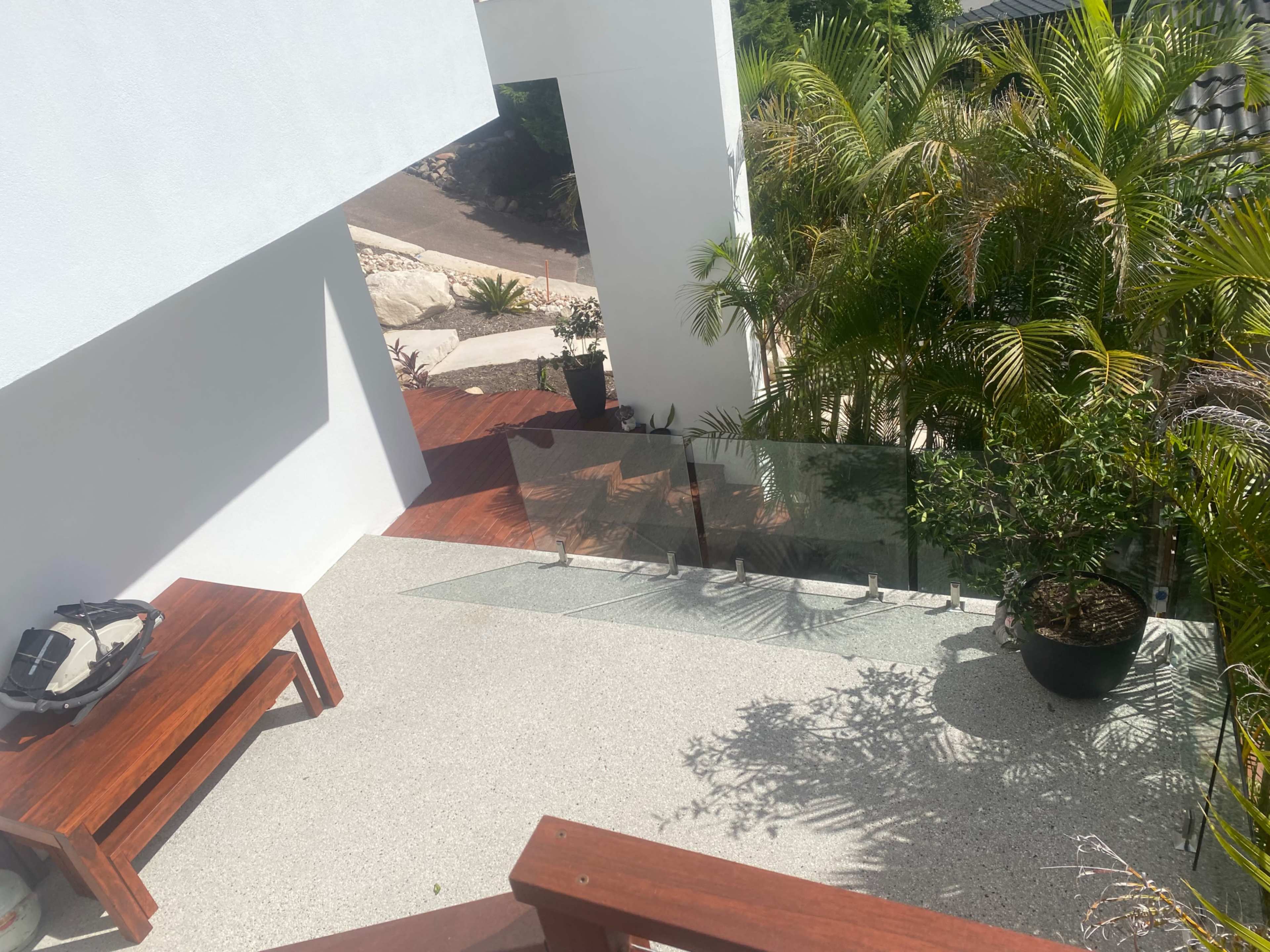 A staircase leading down from a white building to a garden area with tropical plants and wooden decking.