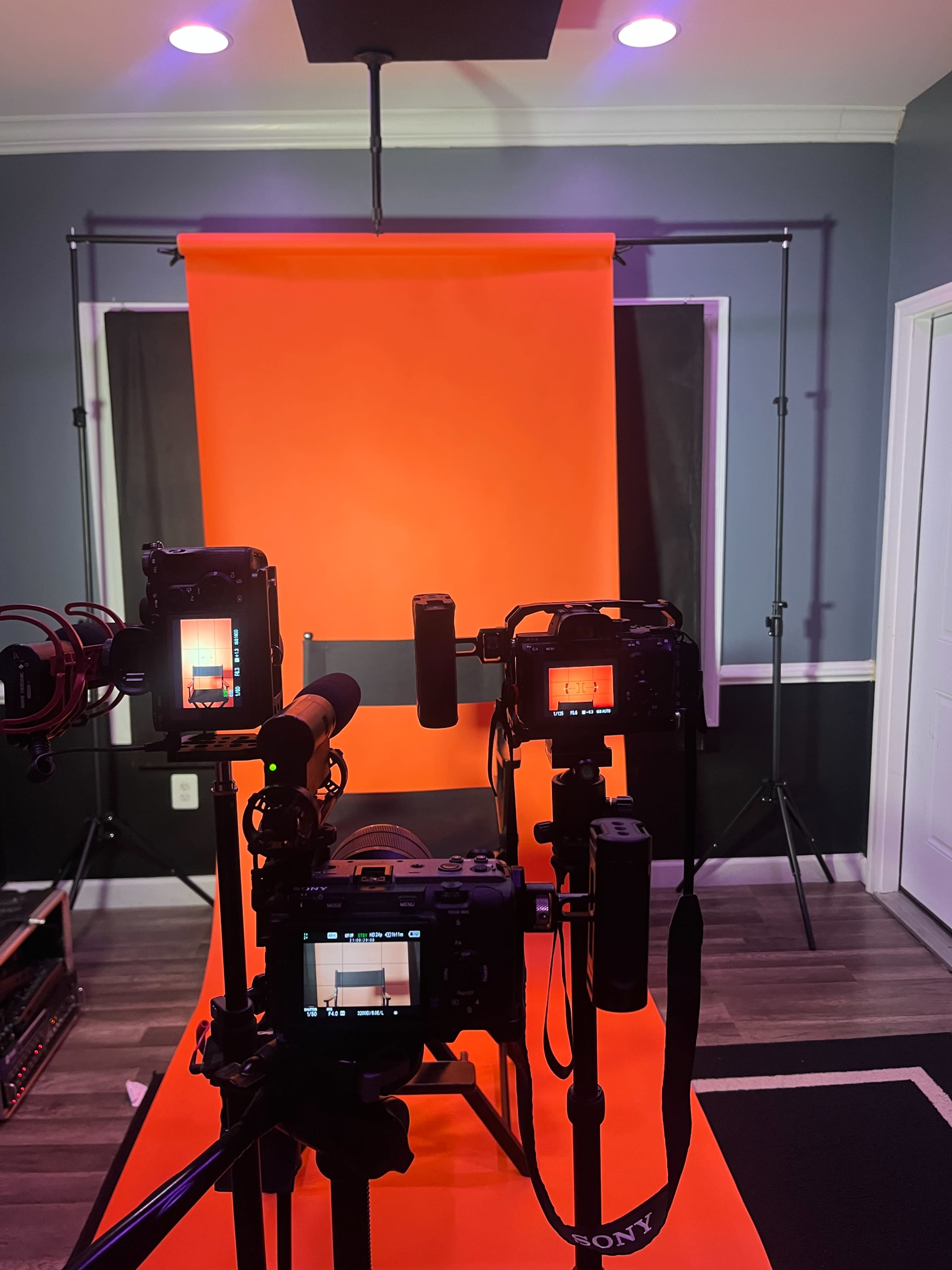 Several cameras and audio equipment set up in front of an orange backdrop in a studio environment.