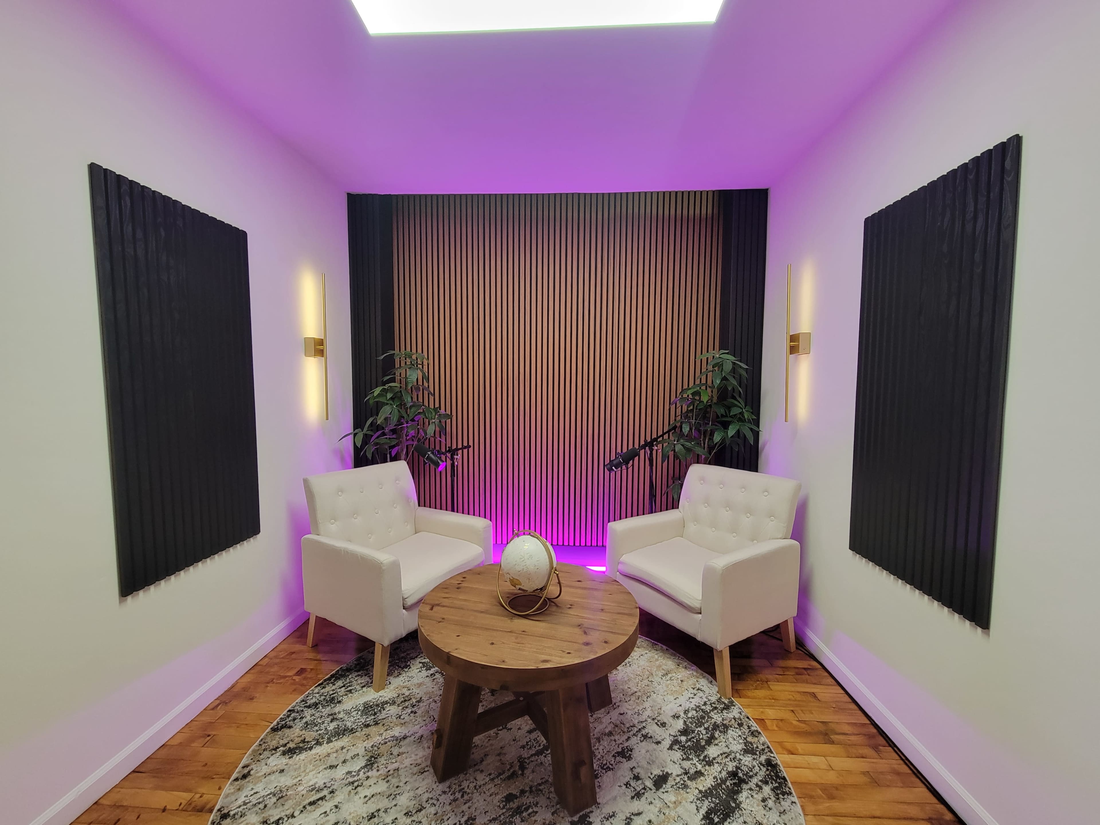 The image shows a modern interior space with two white chairs facing a round wooden table, framed by decorative wall panels and ambient purple lighting.