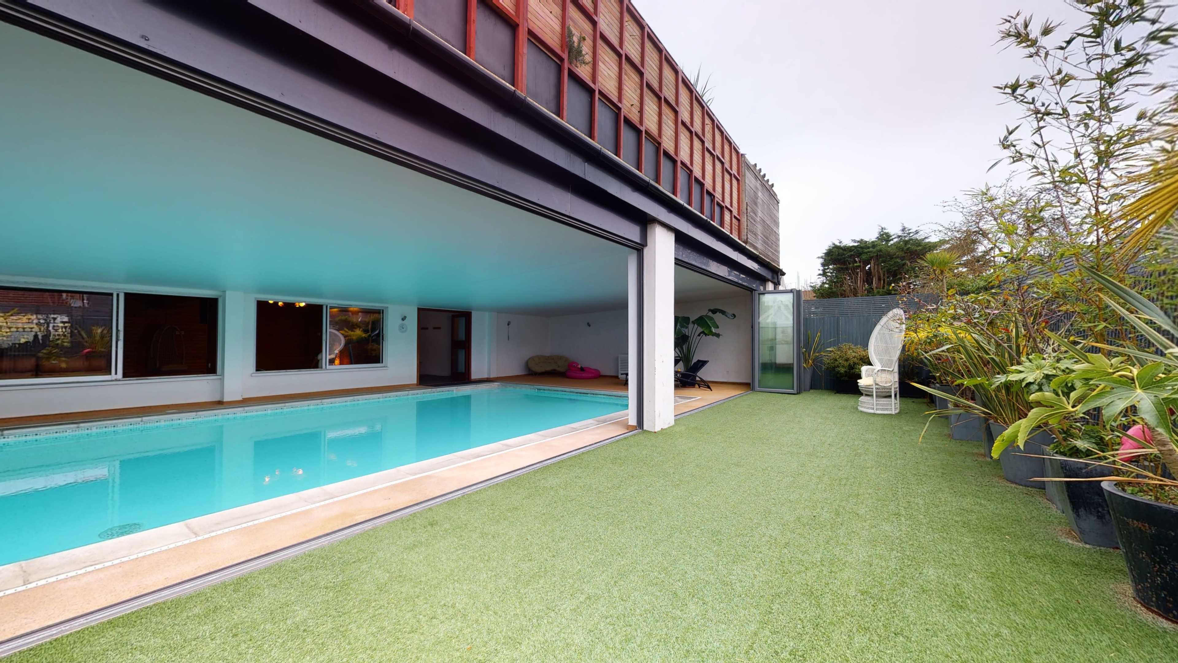The image shows a modern indoor pool area with a grassy outdoor space and a statue surrounded by plants.