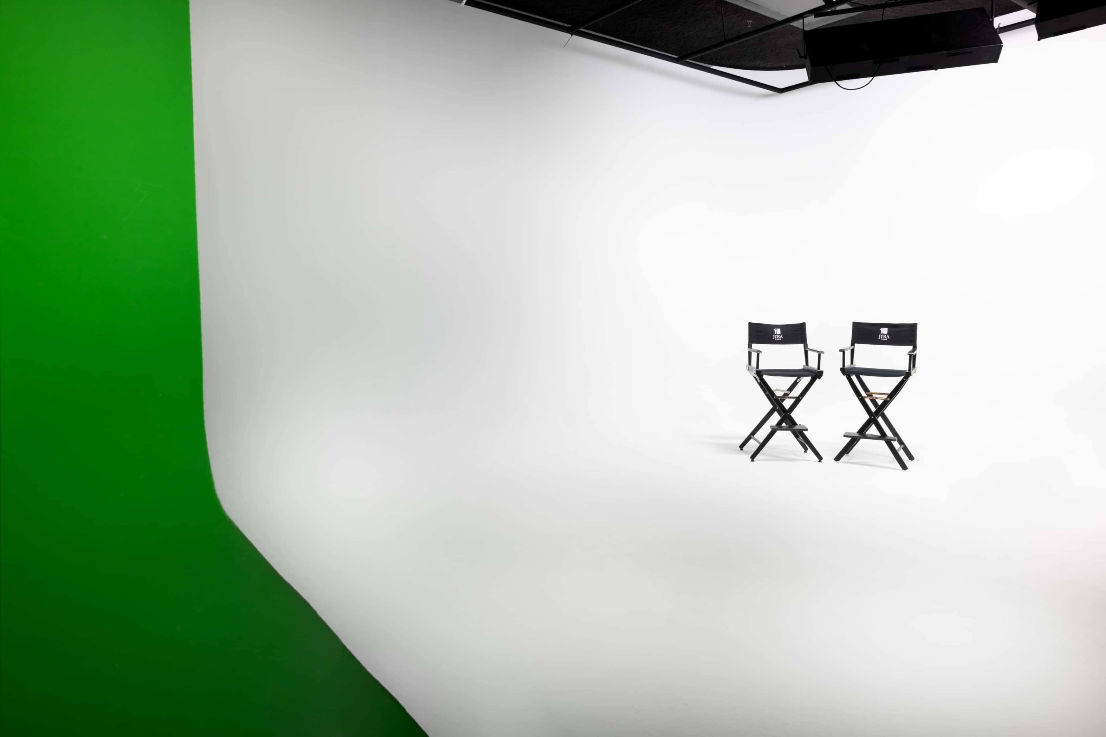 Two black director's chairs positioned on a white backdrop with a green screen on one side.