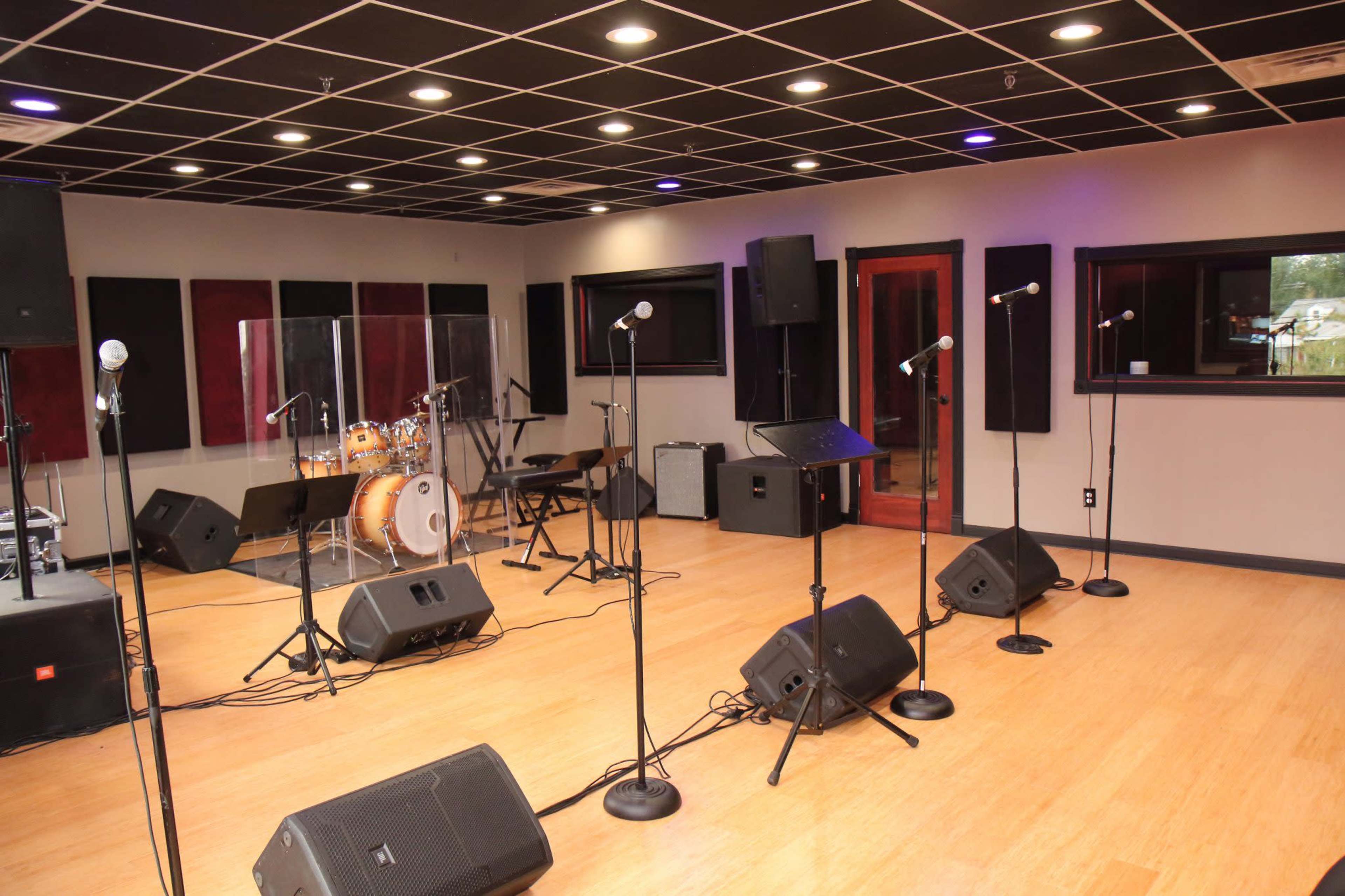 A music rehearsal studio is equipped with microphones, speakers, a drum set, and sound-absorption panels on the walls.