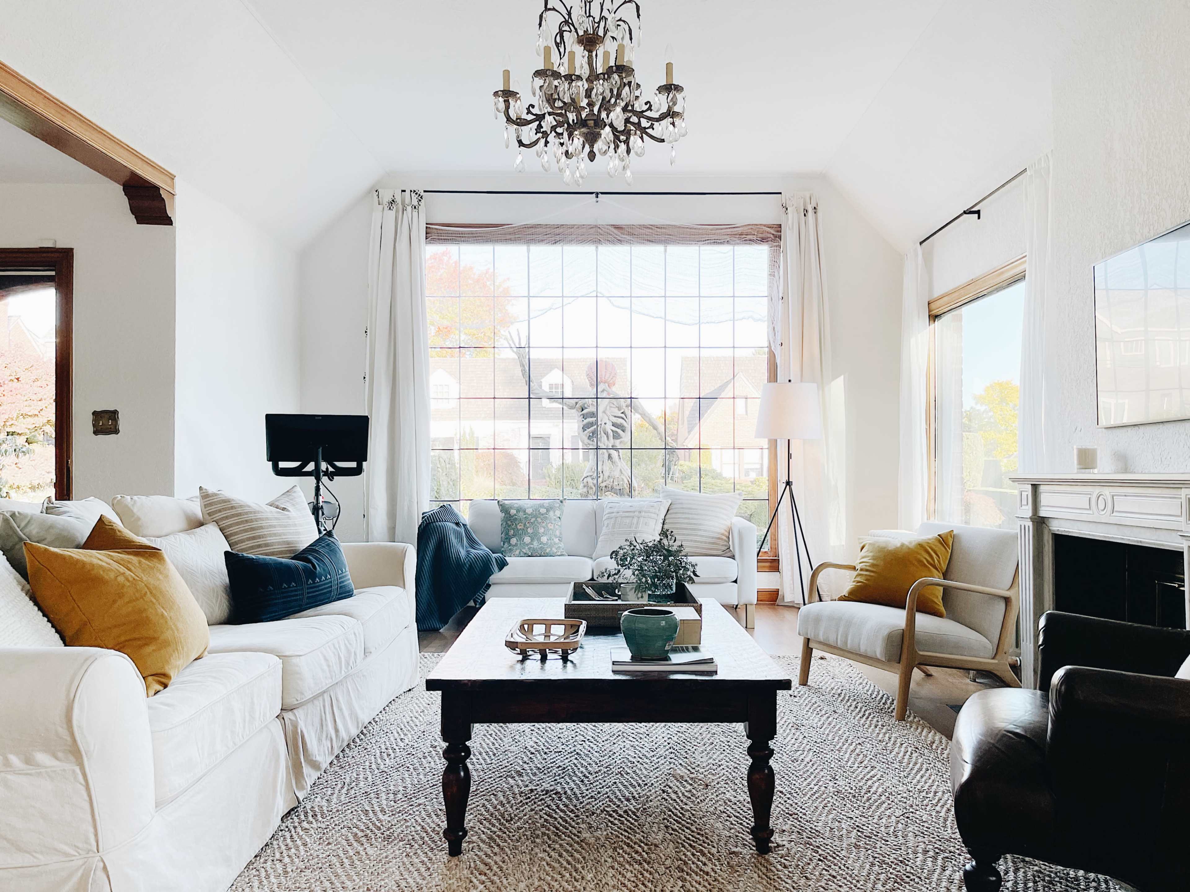 A well-lit living room featuring white sofas, a wooden coffee table, and a large window with a view of a garden.