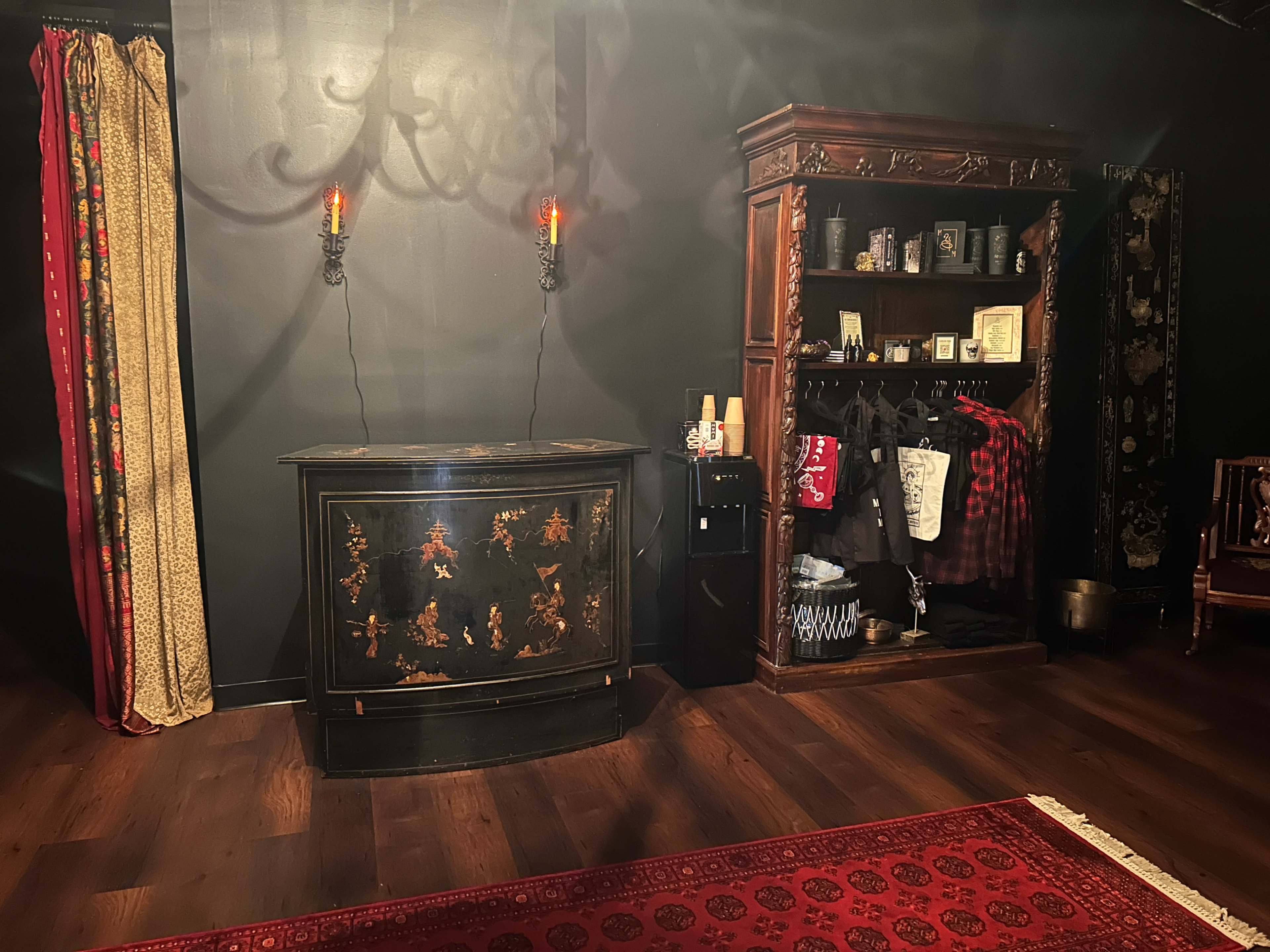 The room features a dark wall, an ornate cabinet with decorative details, two candle sconces, and a wardrobe displaying clothing items.