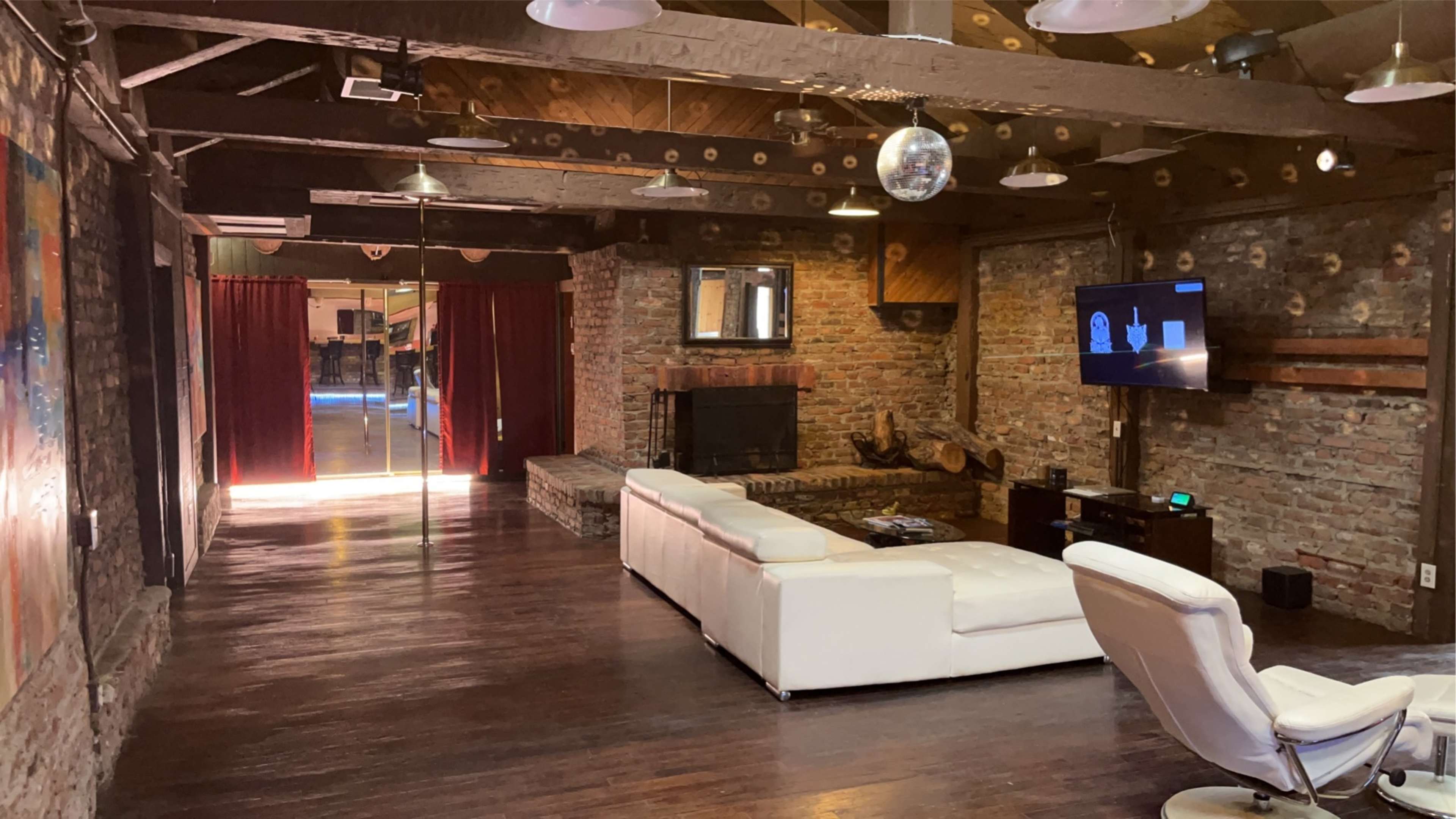 A spacious, rustic room with brick walls, wooden beams, a white sofa, and a television against one wall.