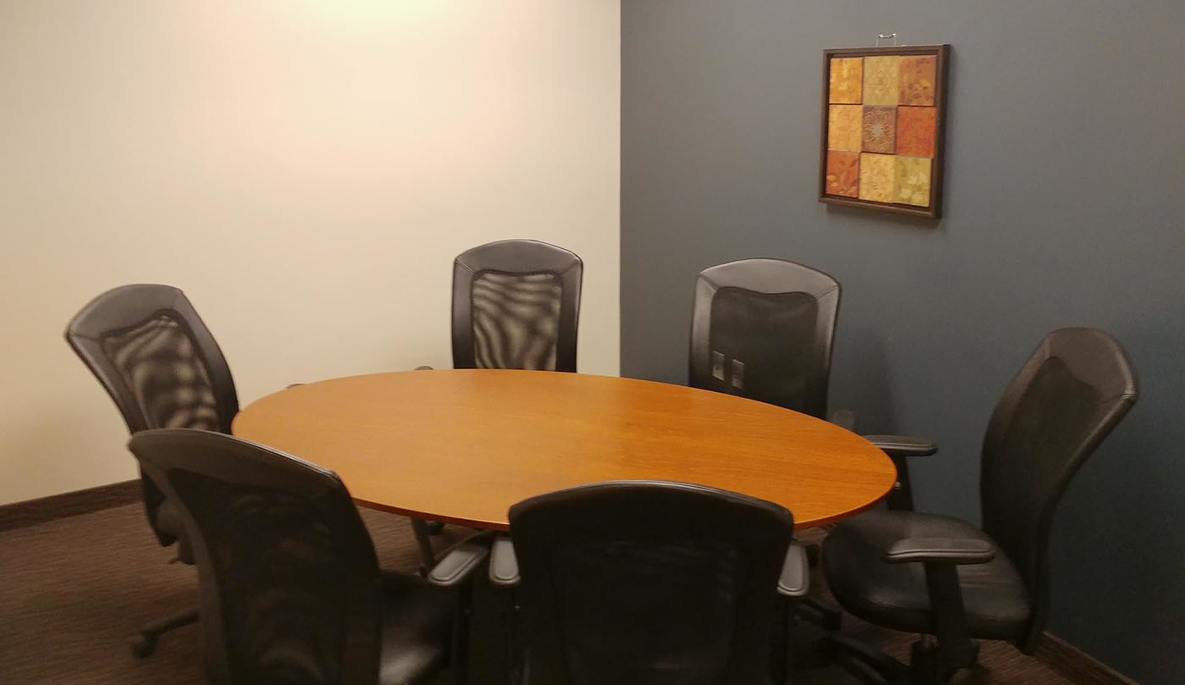 A round wooden conference table is surrounded by six black office chairs in a small meeting room.