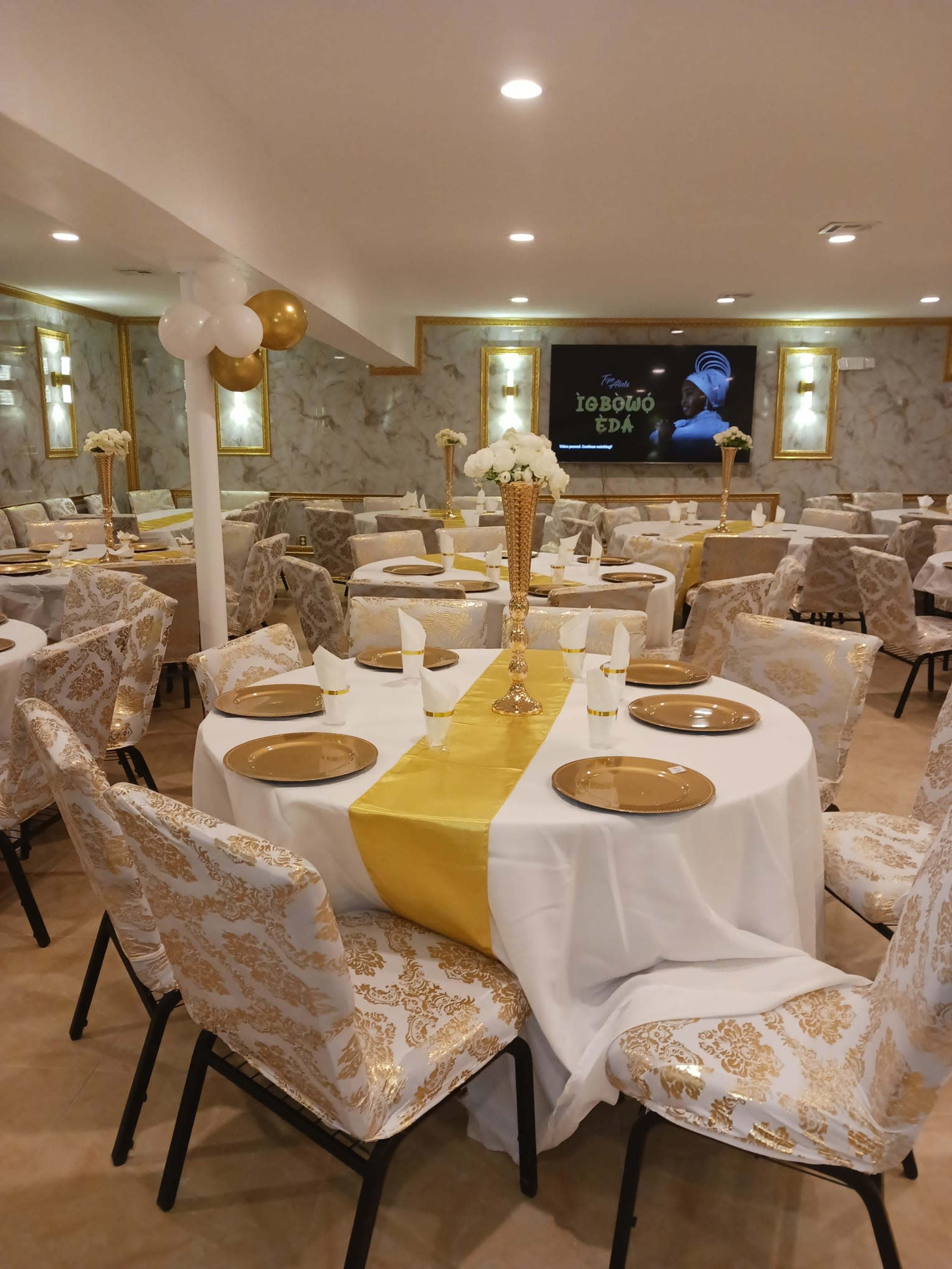A well-decorated banquet hall with tables set for an event, featuring white and gold table linens and chairs.