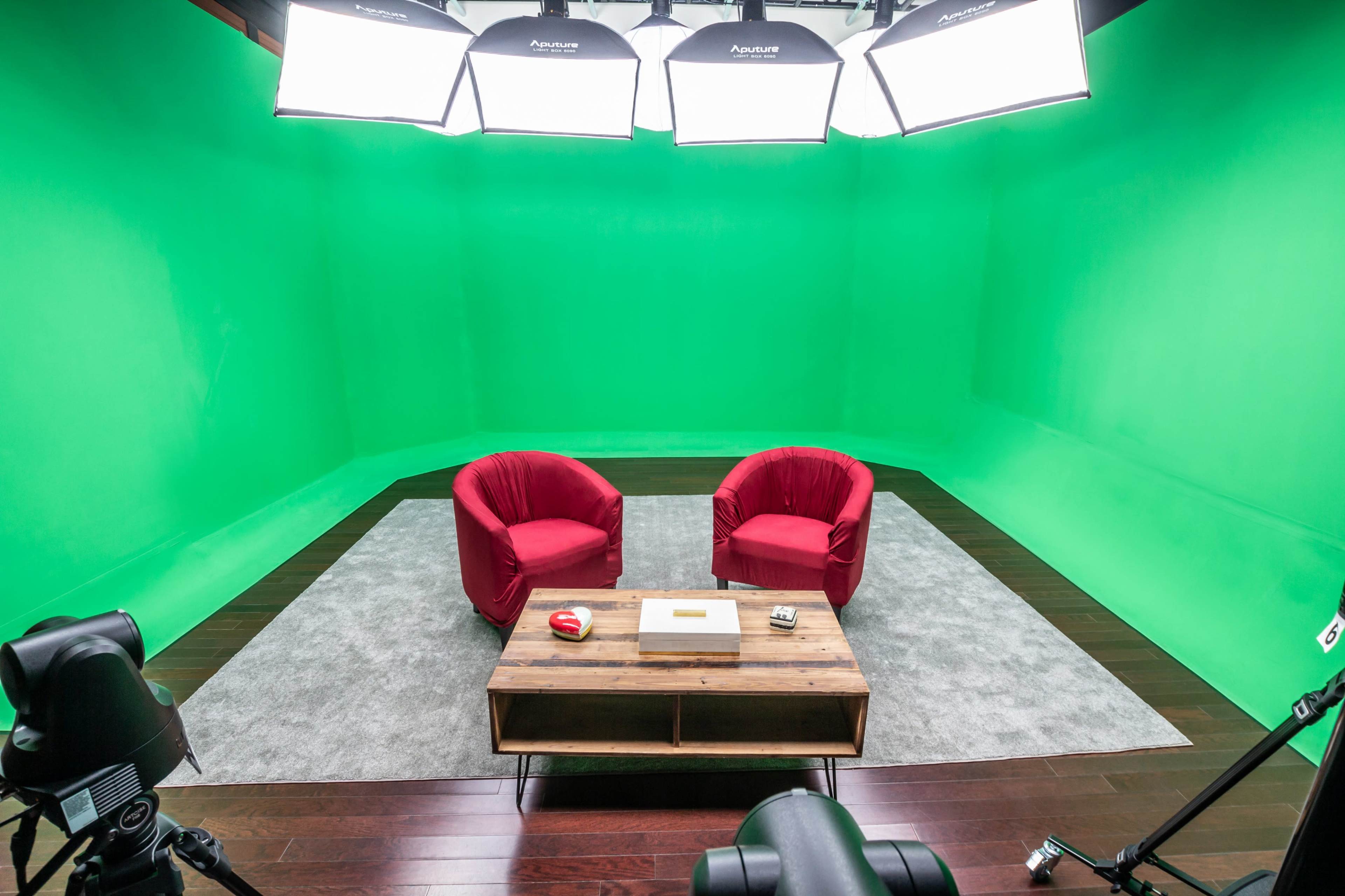 A green screen studio featuring two red chairs facing a wooden coffee table, with multiple lights mounted above.