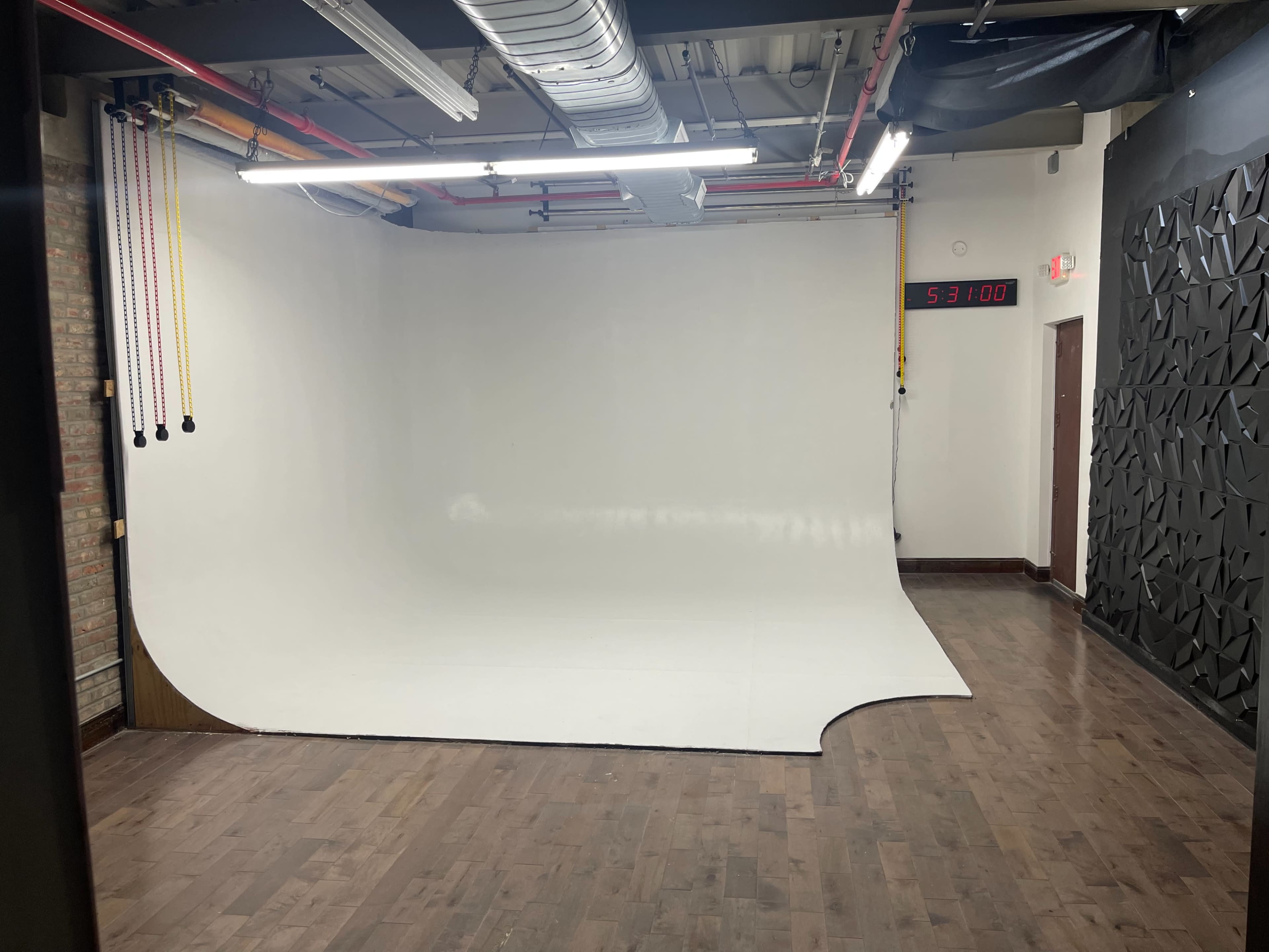 A minimalistic photo studio with a large white seamless backdrop and wooden flooring.