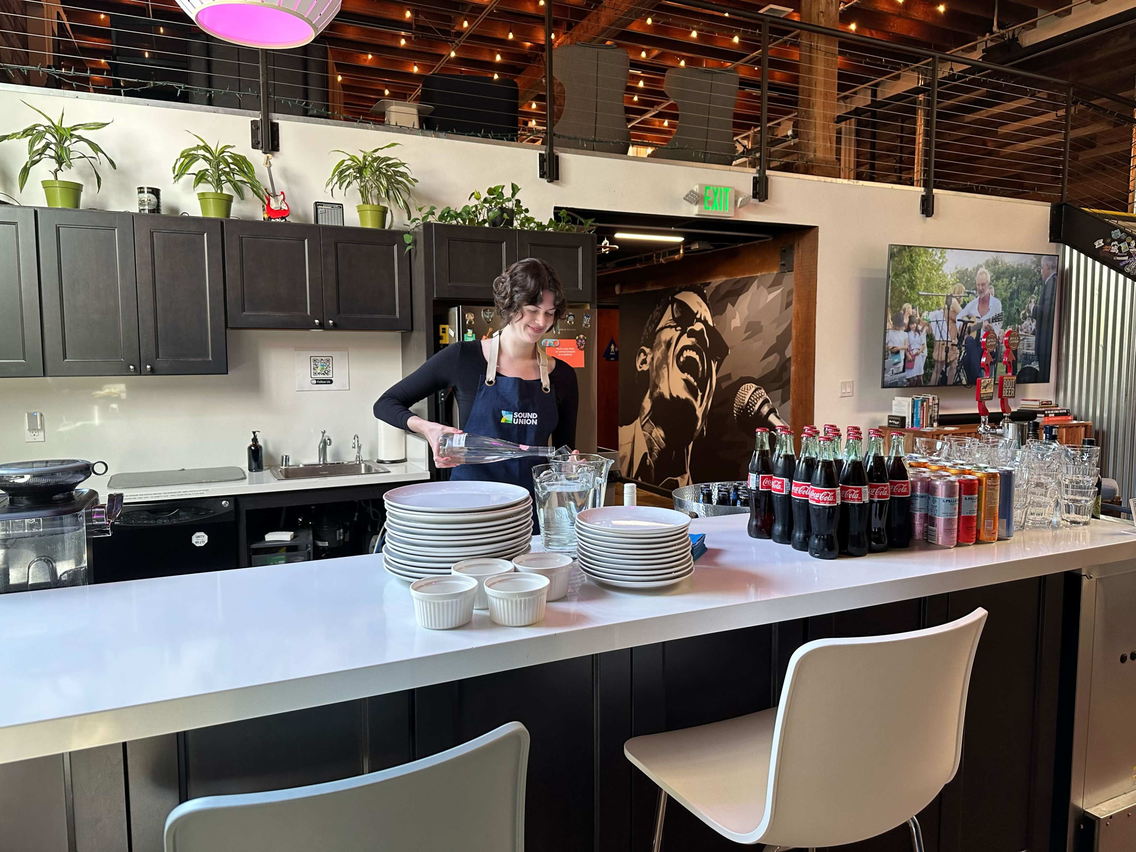 A barista prepares drinks behind a well-organized counter filled with glassware and beverages.