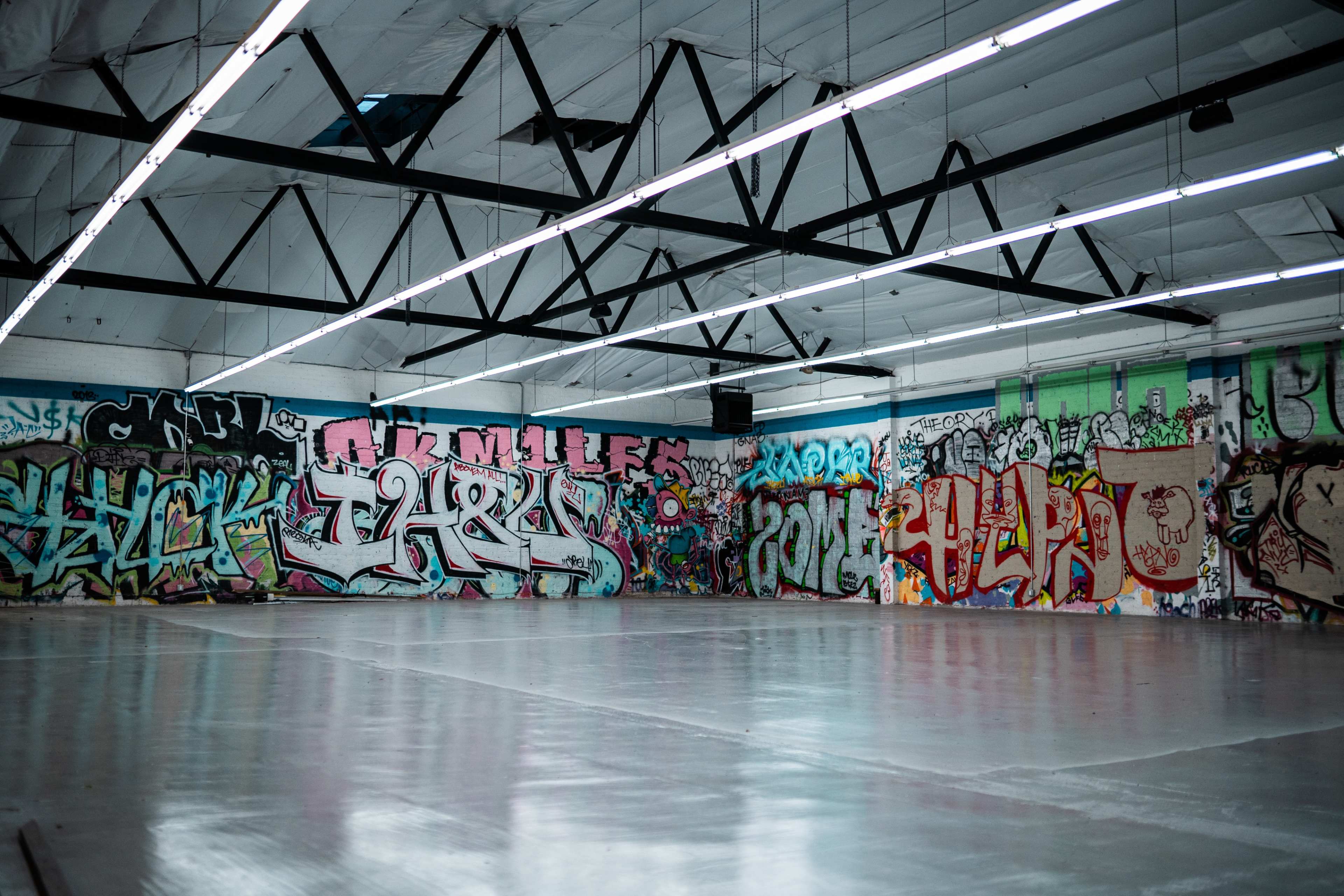 An industrial space with bare concrete flooring and walls covered in various styles of colorful graffiti.
